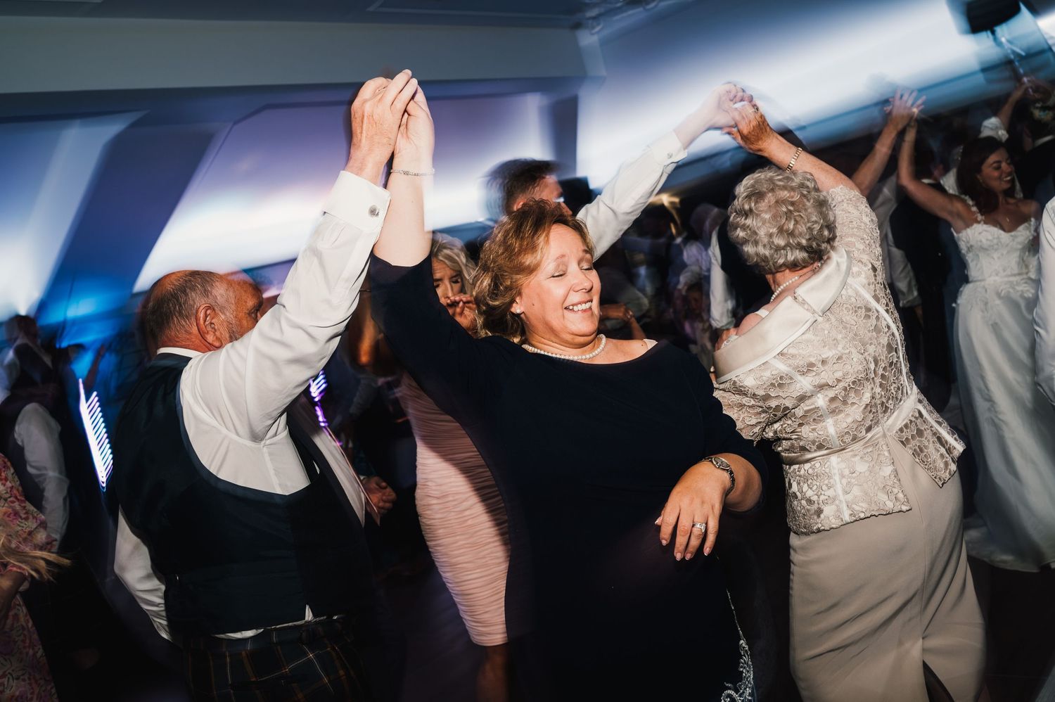 Wedding guests dancing and celebrating with raised arms on dance floor.