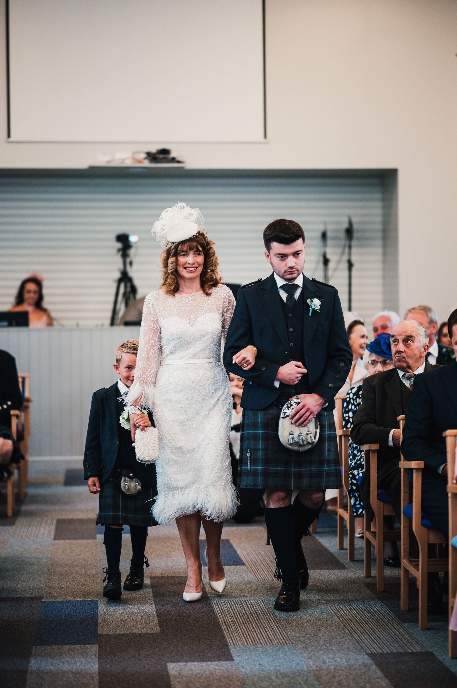 Wedding party walks down church aisle with young ring bearer in Scottish-themed ceremony.