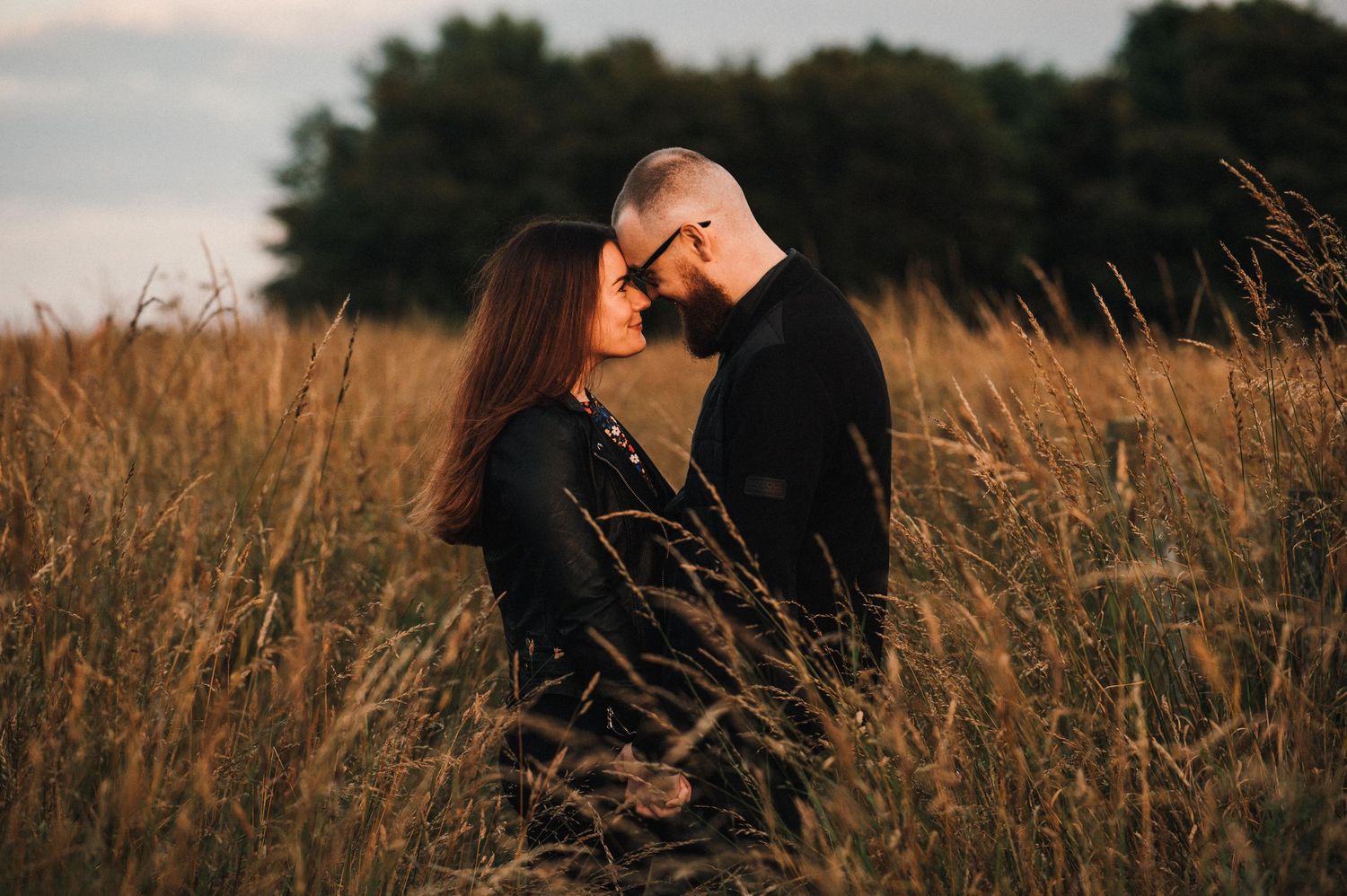 A romantic couple embraces in a golden wheat field at sunset creating an intimate silhouette against nature.