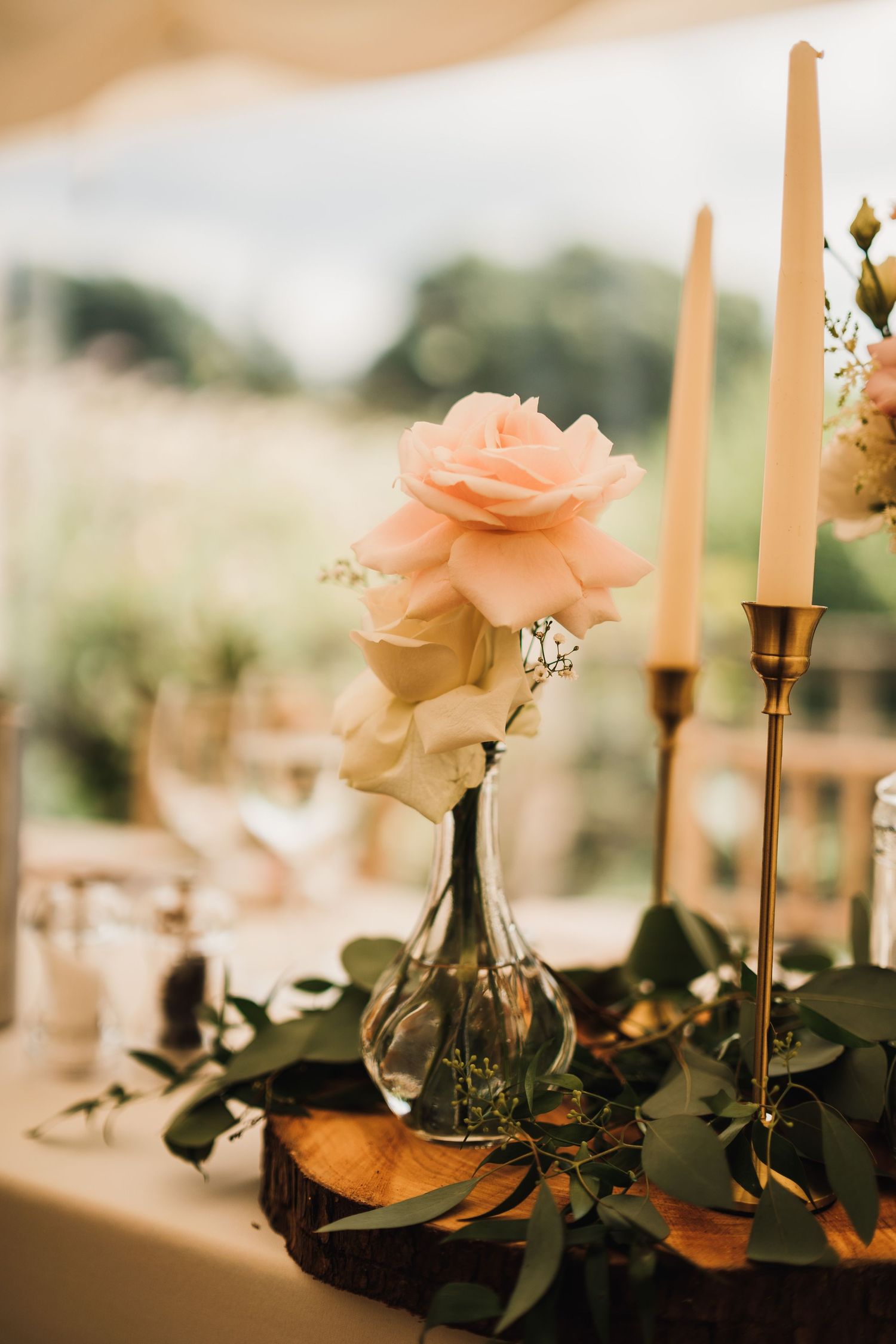 Delicate peach rose in glass vase with tall taper candles and greenery table decor.