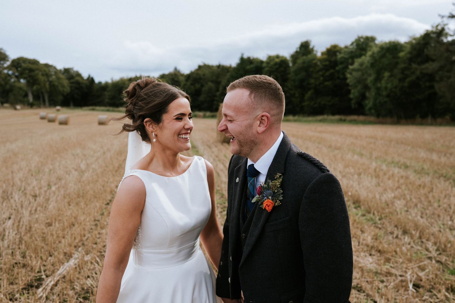A joyful couple shares a laugh in a golden wheat field during their Scottish wedding.
