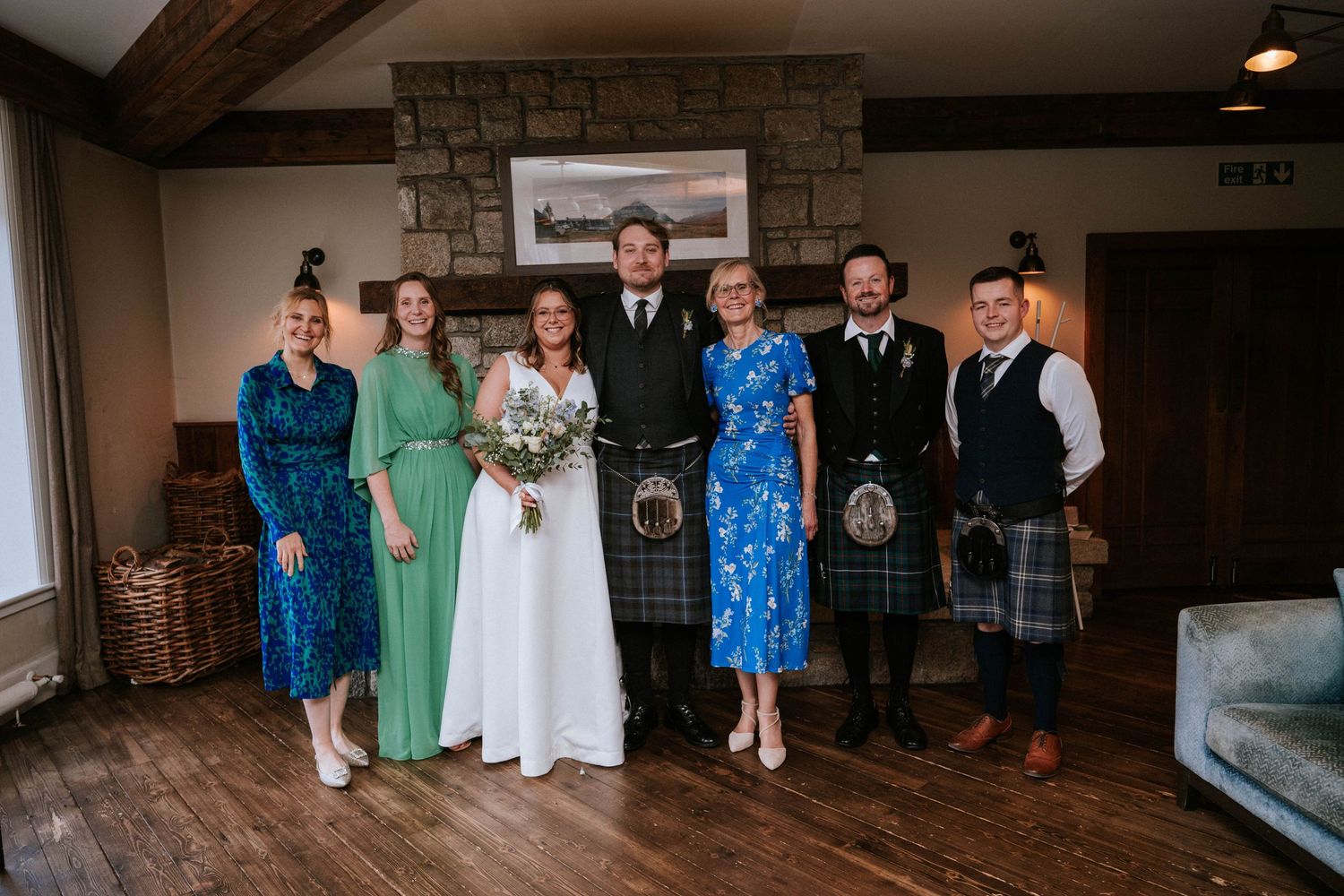 Wedding party poses in a rustic stone-walled venue with elegant dresses in blue and mint green tones.