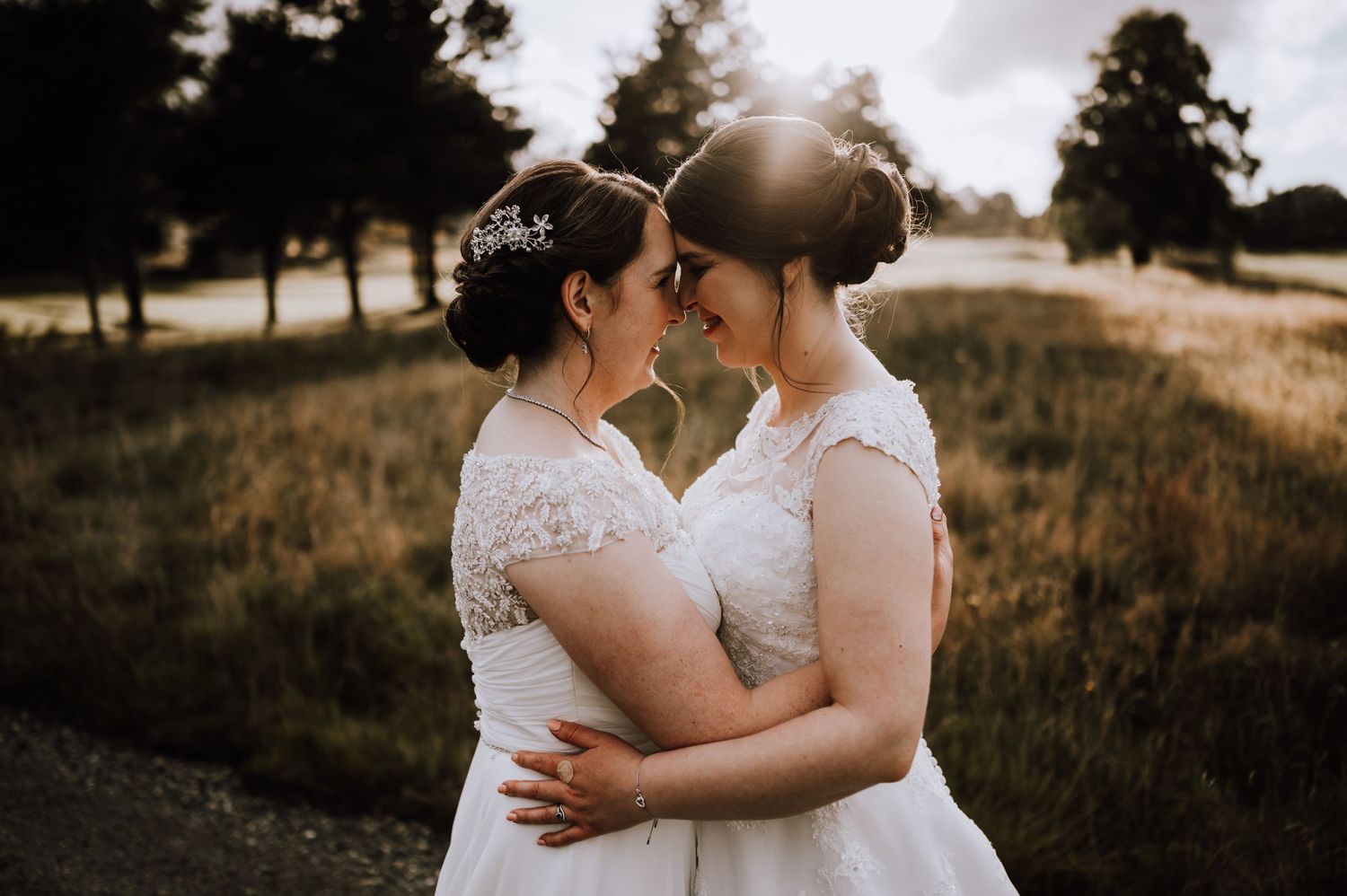 Intimate moment between newlyweds in white dresses during sunset photoshoot.