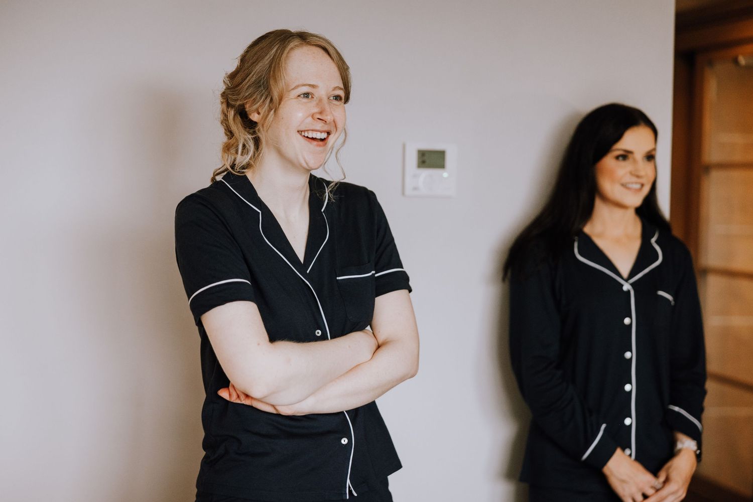 Two people in matching black and white piped pajamas stand against a white wall.