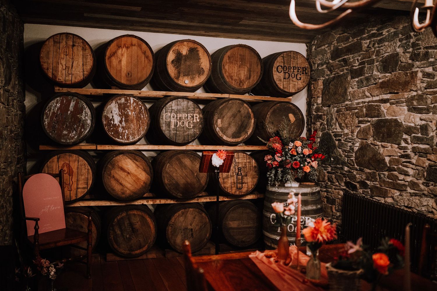 Rustic wine cellar with wooden barrels stacked against a stone wall and red table decorations.