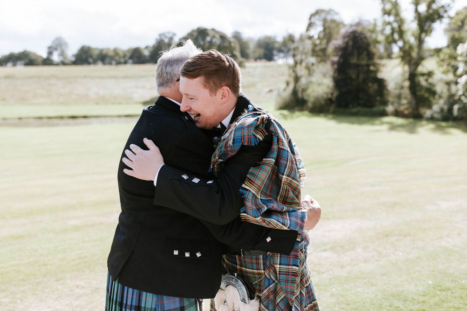 Heartfelt embraces between wedding party members on a sunny castle lawn.