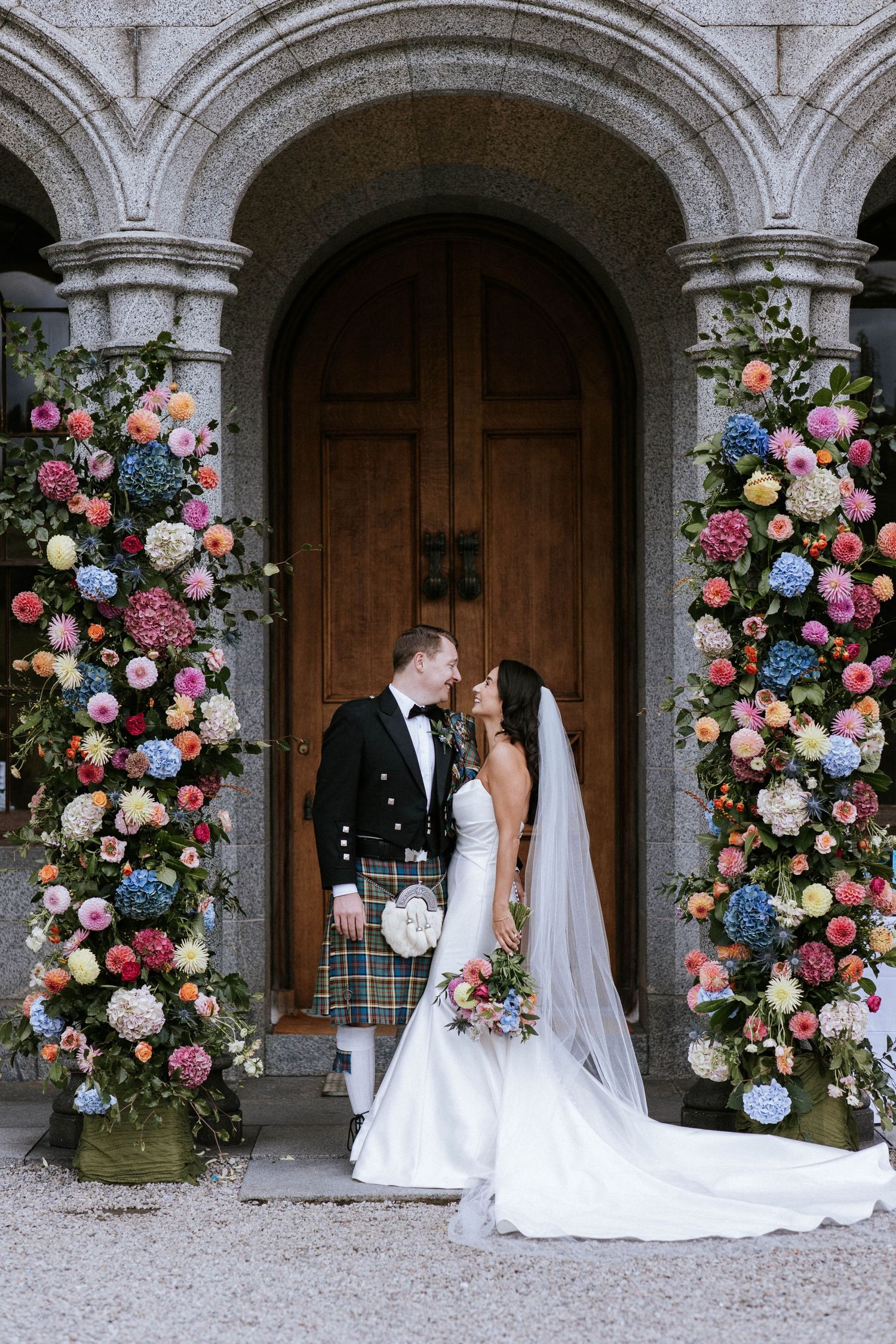 Ornate floral arrangements frame a wooden doorway arch with pink and white roses.