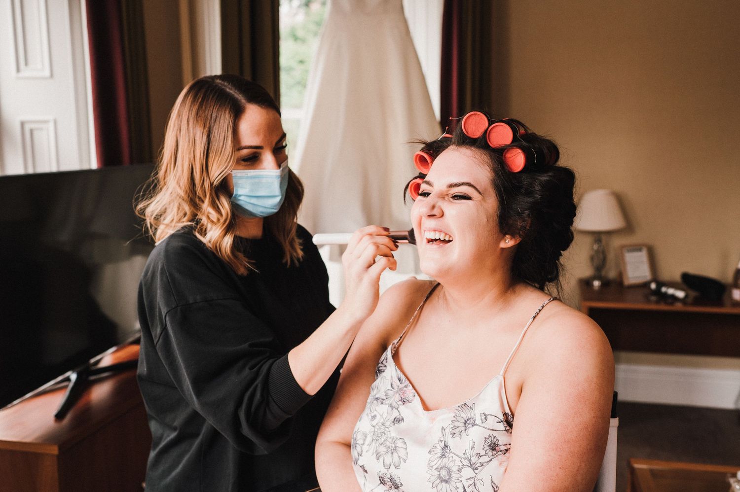 Wedding preparation scene showing makeup application during pandemic with masks.