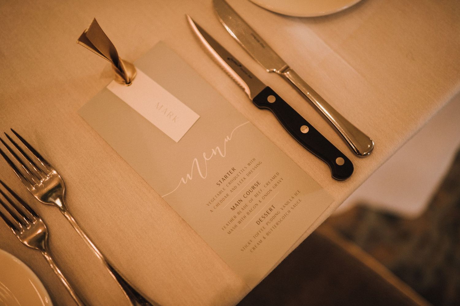 Elegant place setting with silverware, menu card, and name tag at wedding reception.