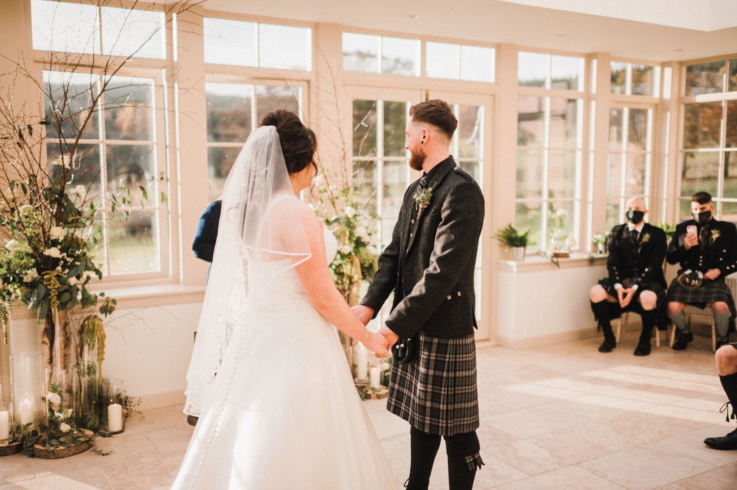A Scottish wedding ceremony in a bright conservatory with traditional kilts and formal wear.