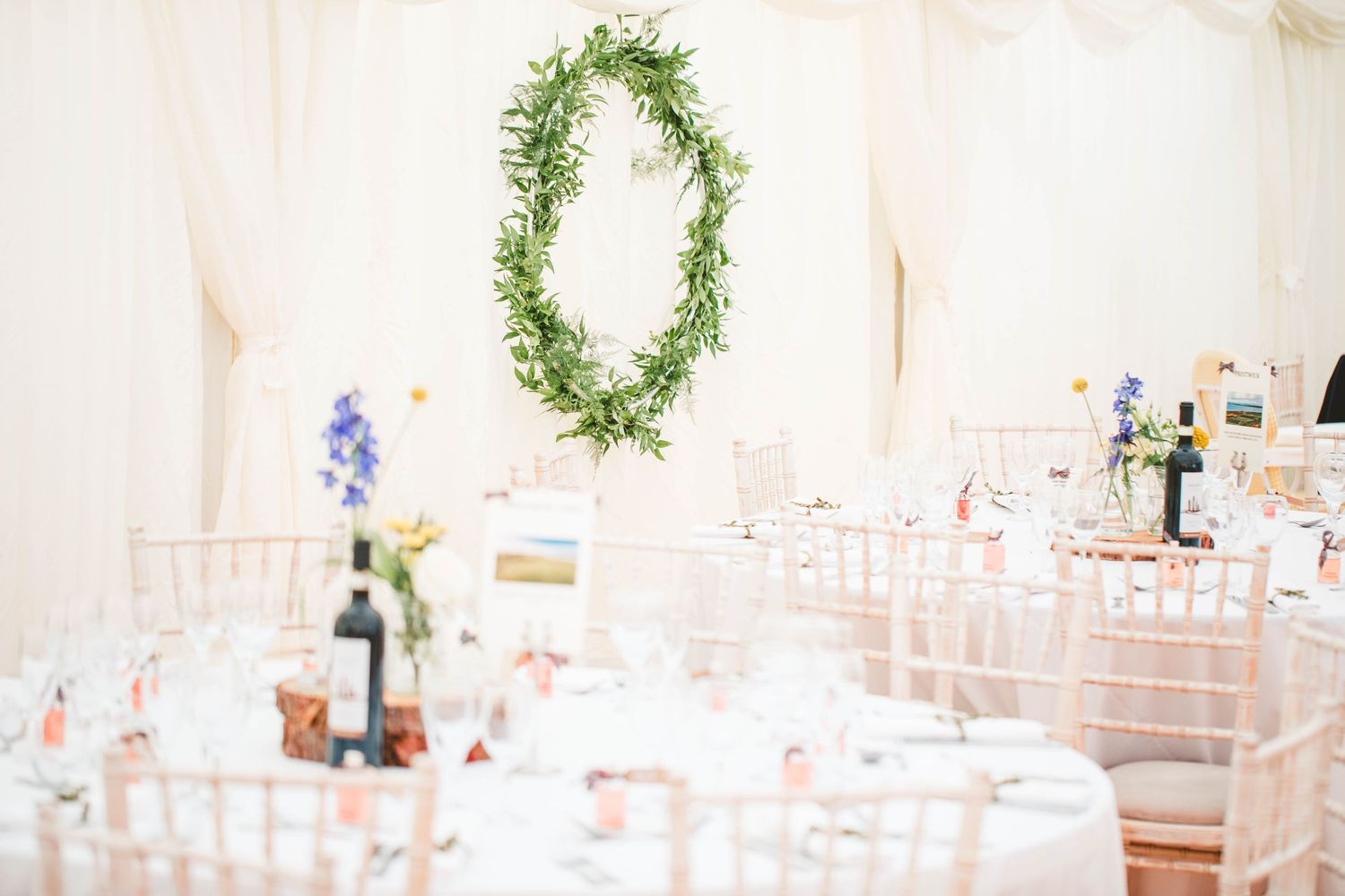Elegant wedding reception setup with greenery wreath decoration and pink chiavari chairs.