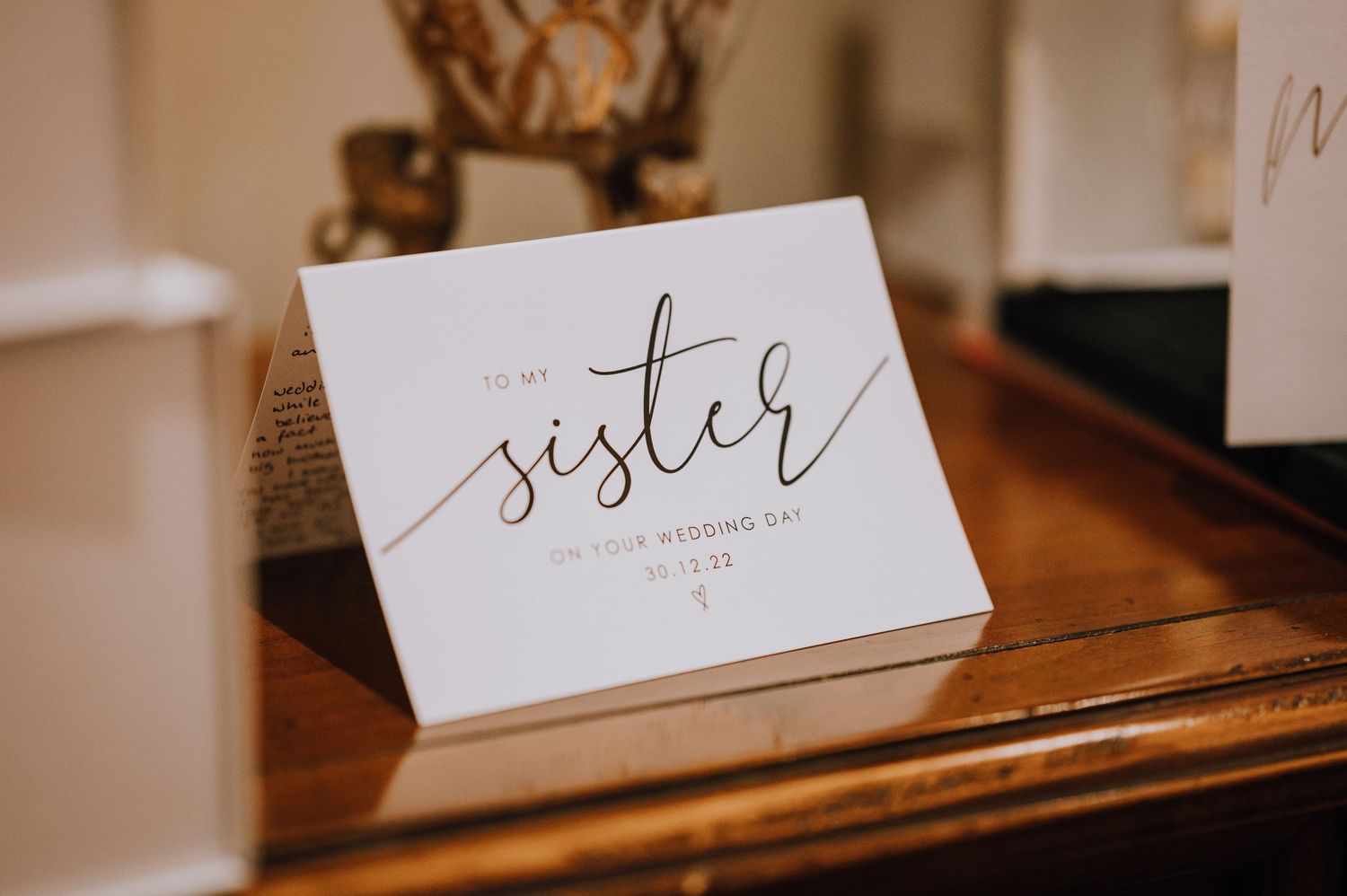 A white card with elegant calligraphy reading 'sister' sits on a wooden surface.