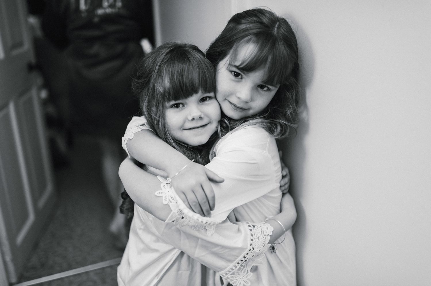 Two young children sharing a warm embrace against white wall.