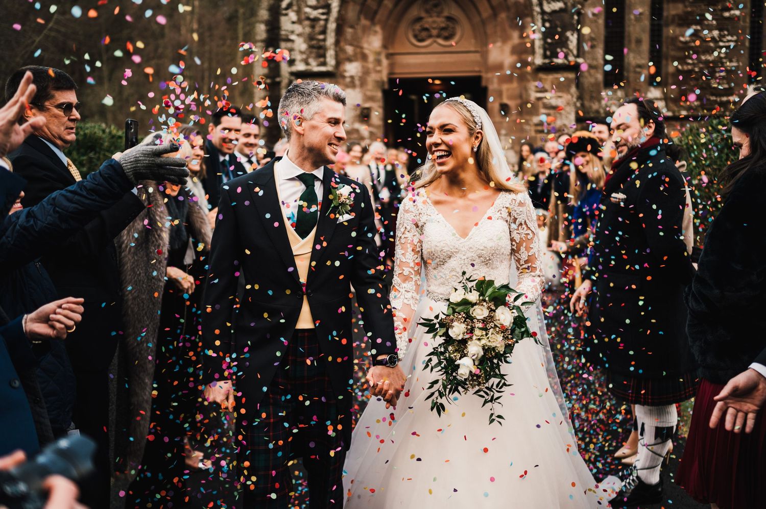 Wedding guests throw confetti over the newlyweds outside a historic church building.