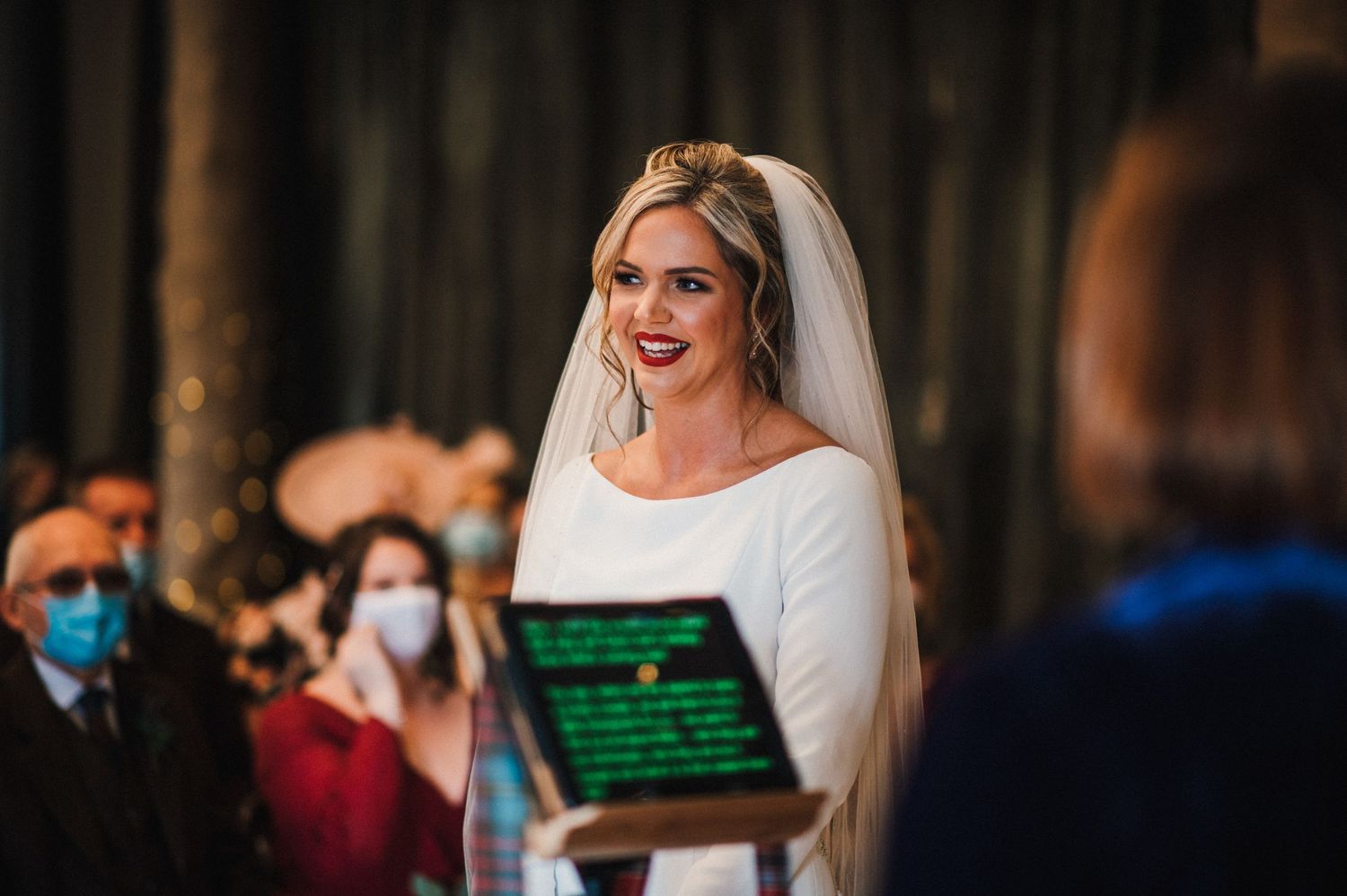 A wedding ceremony in a ballroom with dark curtains and illuminated tablet screens.