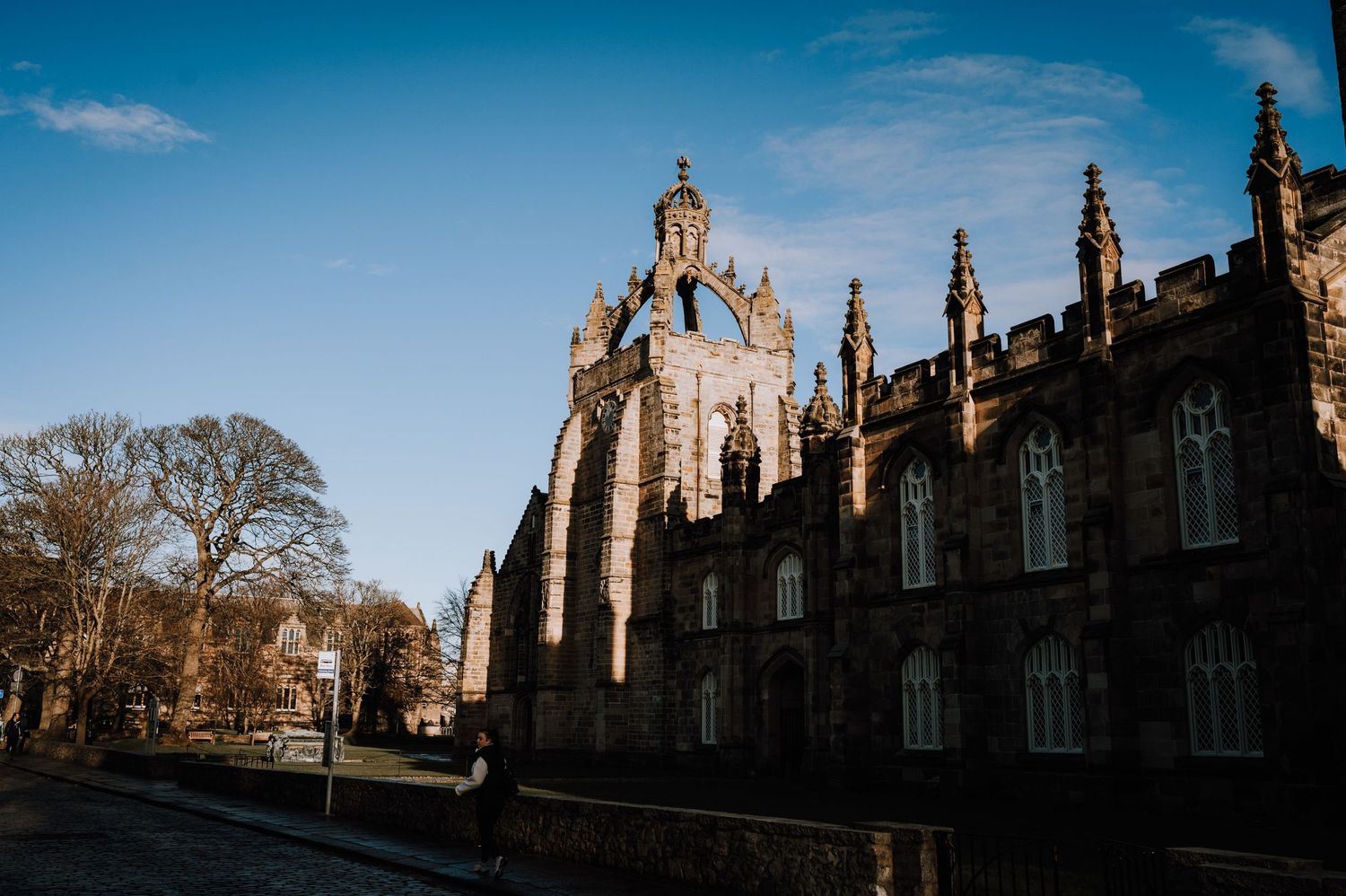 Gothic stone church building with spires under blue sky and bare trees.