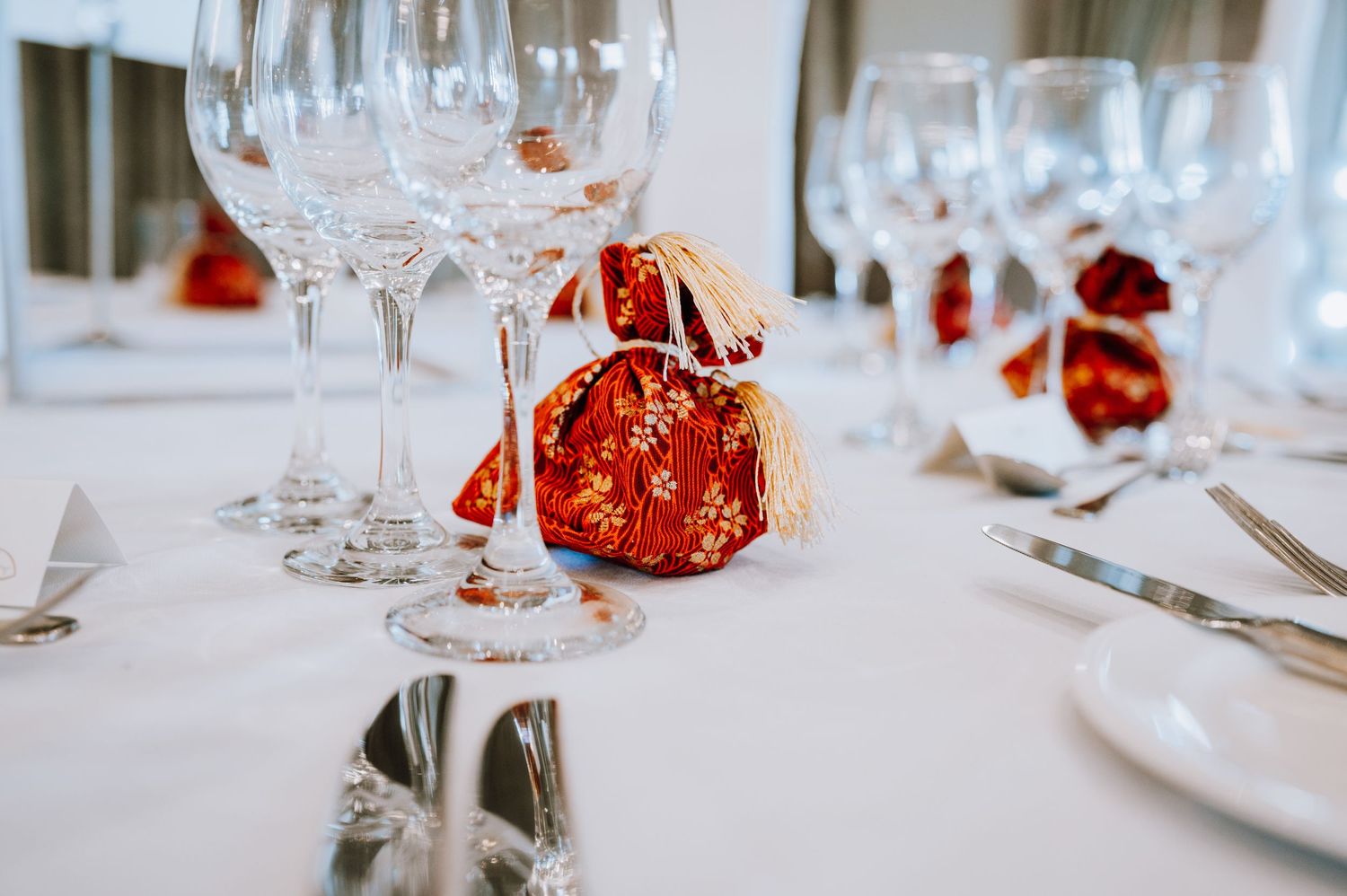 Red ornamental favors and wine glasses set on a formal white tablecloth.