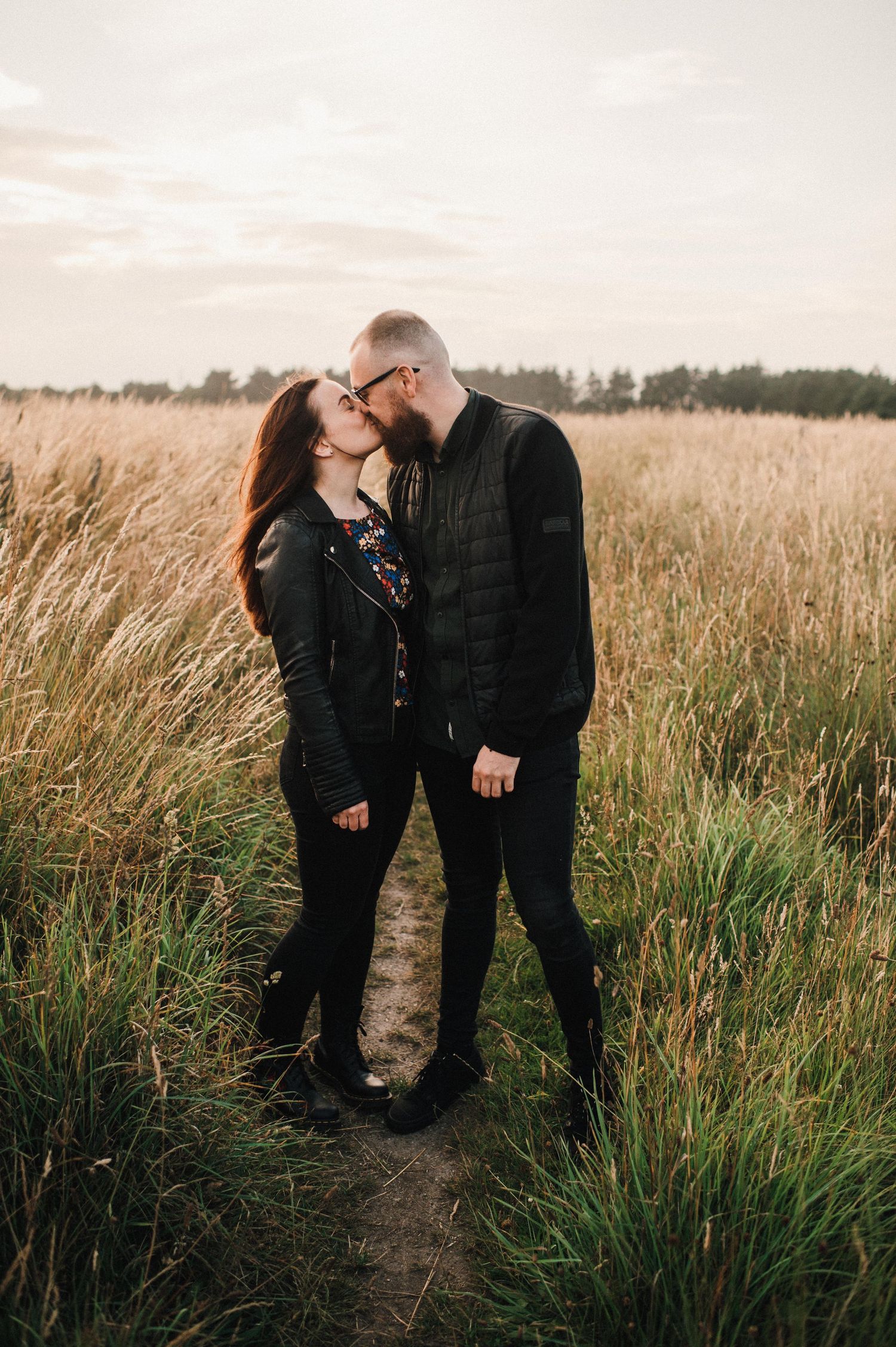Intimate moment shared on dirt path surrounded by tall grass at sunset.