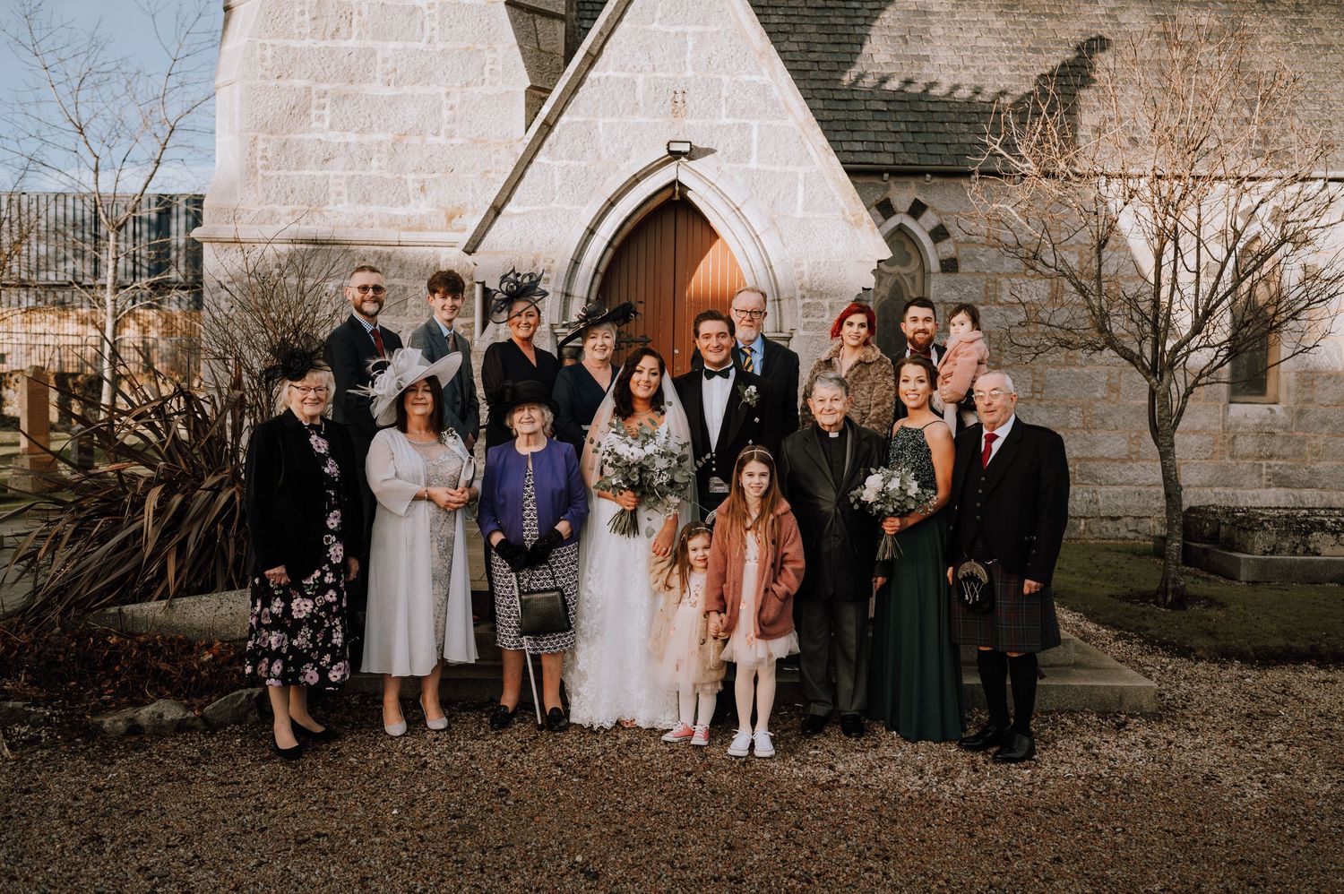 Extended family and wedding guests gather for formal group photo outside church.