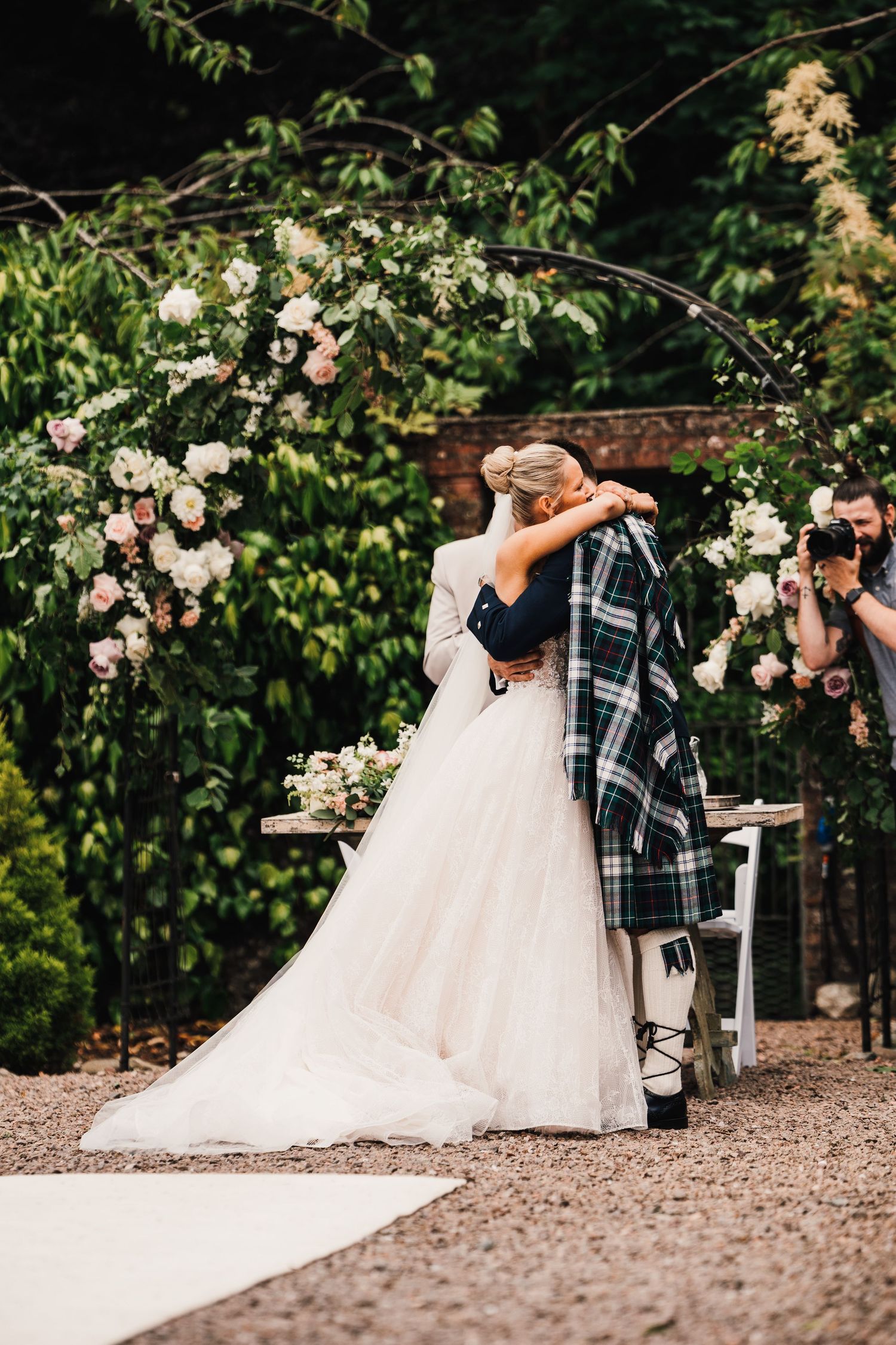 Garden wedding ceremony under floral arch with white roses and greenery.
