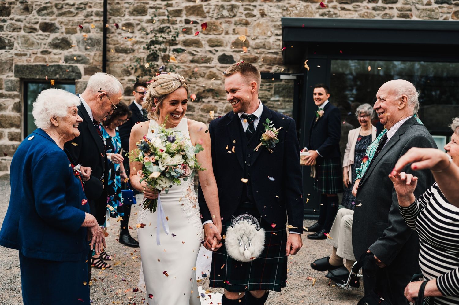 Wedding celebration outside rustic stone building with Scottish traditional dress.