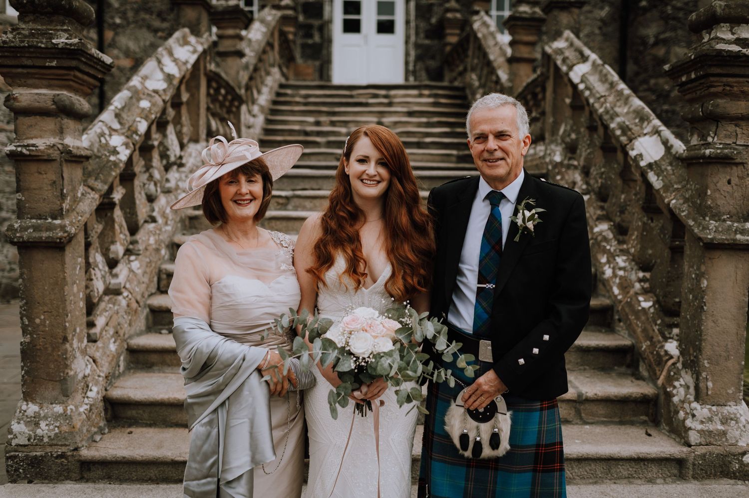 Wedding party posed on ornate stone staircase with traditional Scottish formal wear.