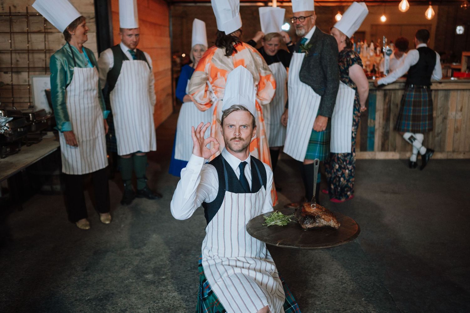 A person in a striped apron poses playfully during a wedding celebration.