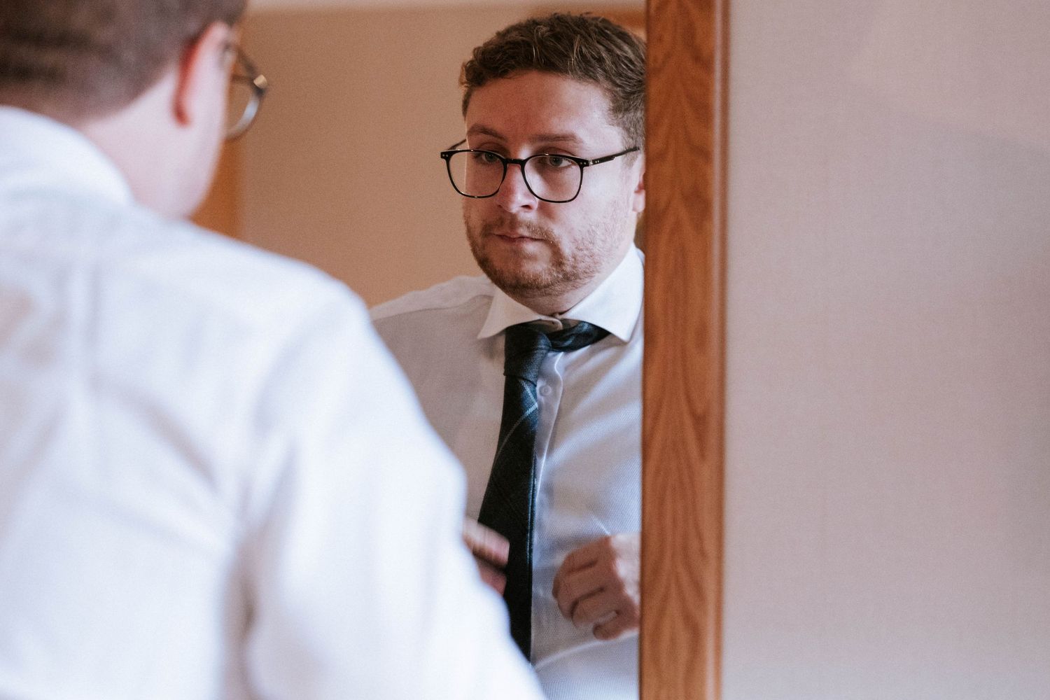 Person adjusting tie in mirror while preparing for formal event.