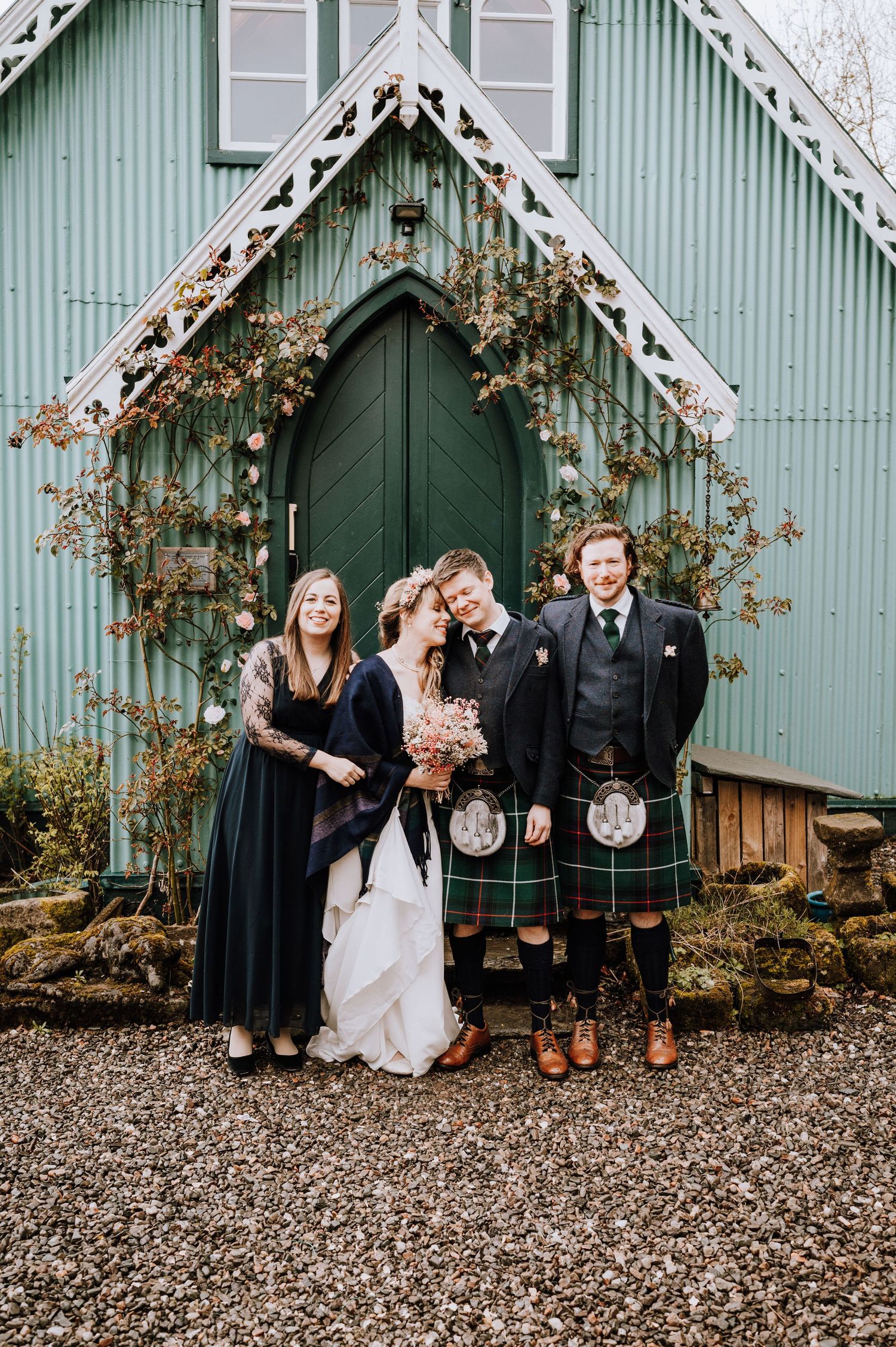 Wedding group in Scottish formal wear stands by mint green church entrance.