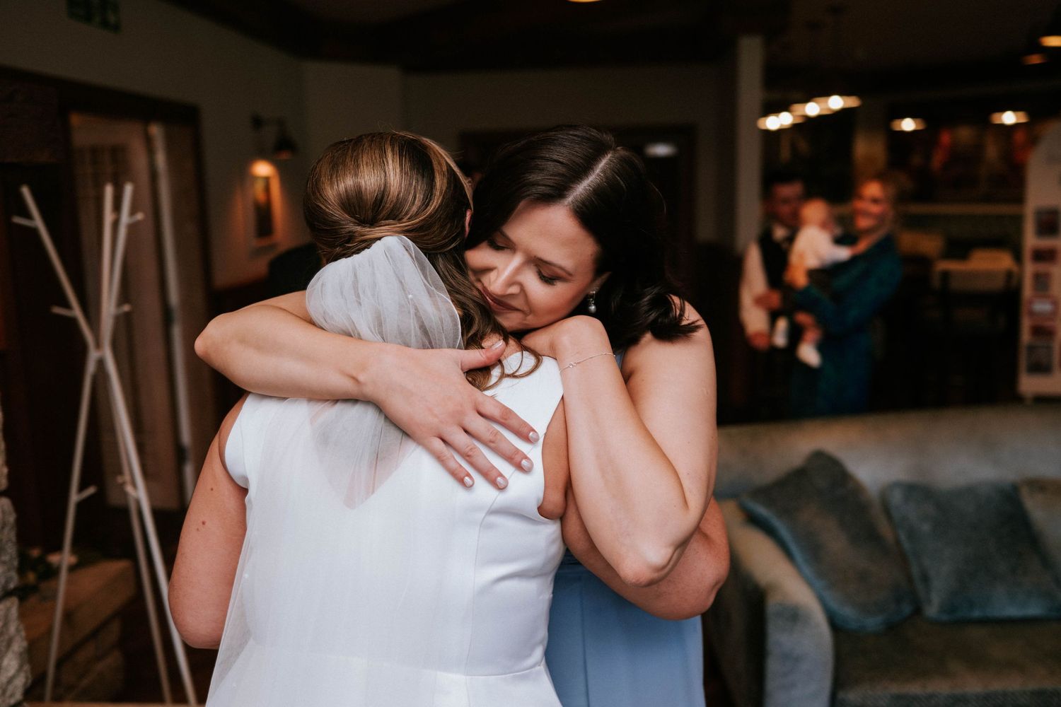 Two people embrace in a tender moment during a wedding celebration at a dimly lit venue.