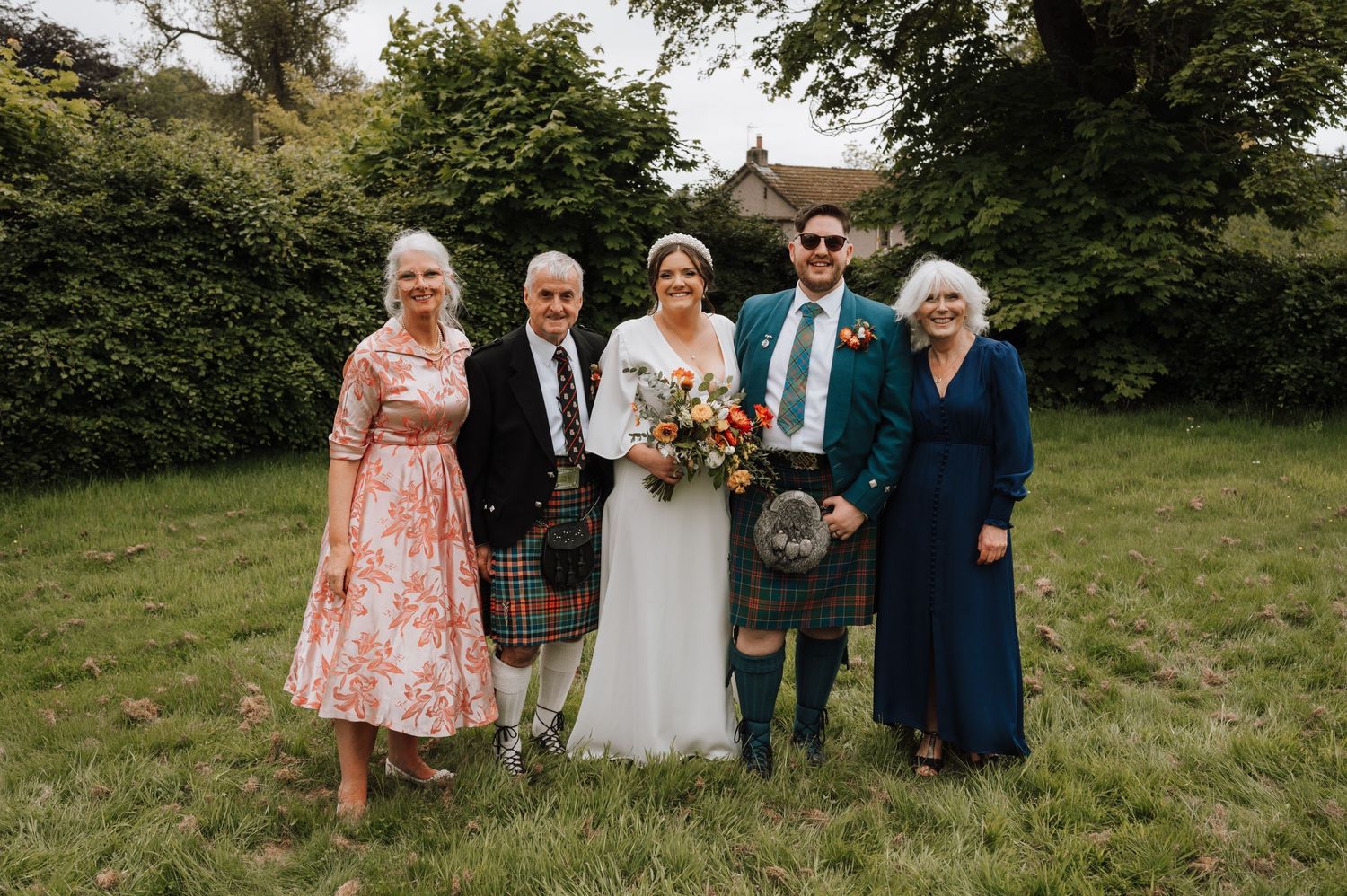 Small family group in traditional Scottish attire poses for formal wedding portrait.