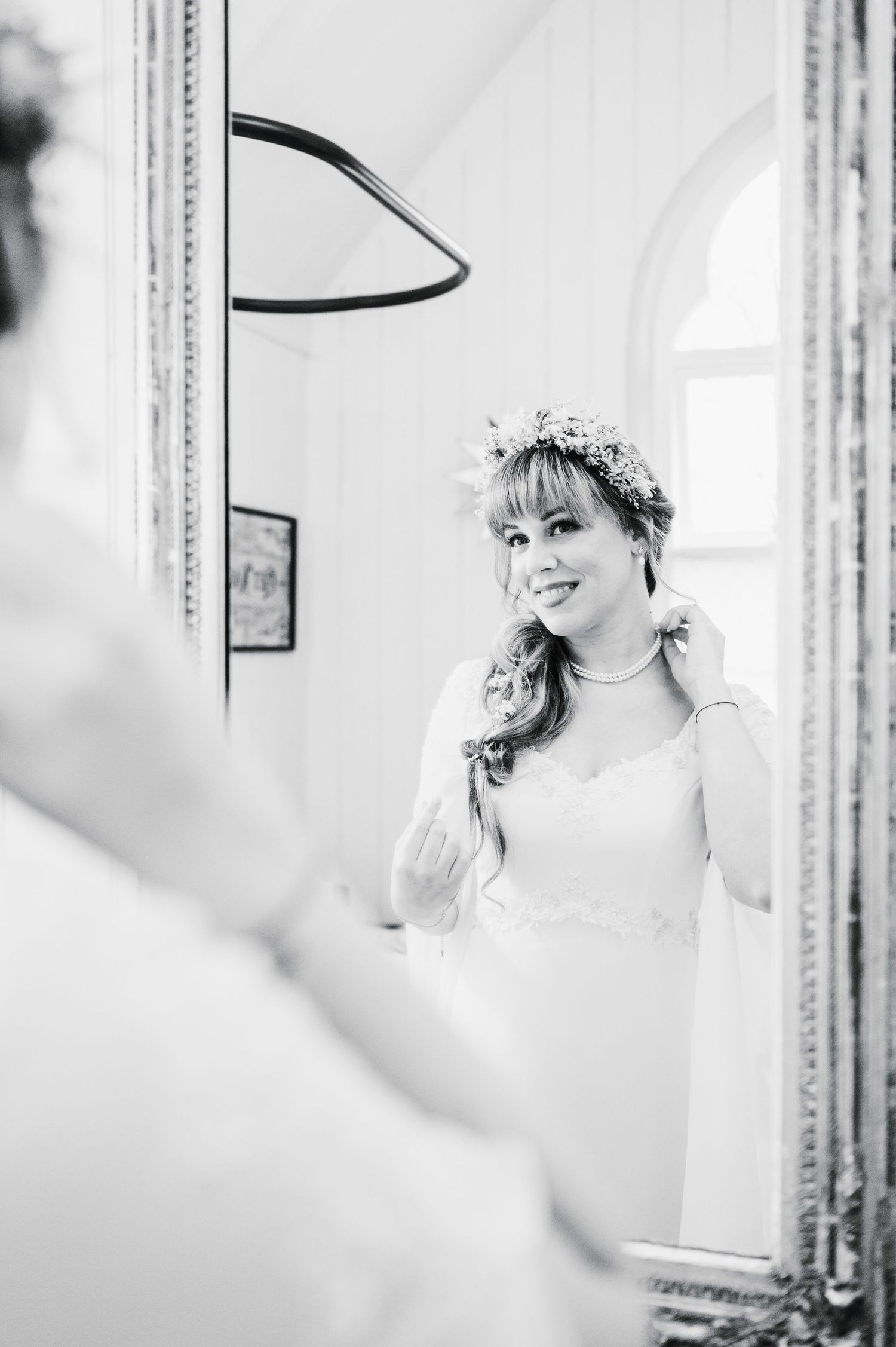 Black and white portrait of bride with floral crown reflected in ornate mirror.
