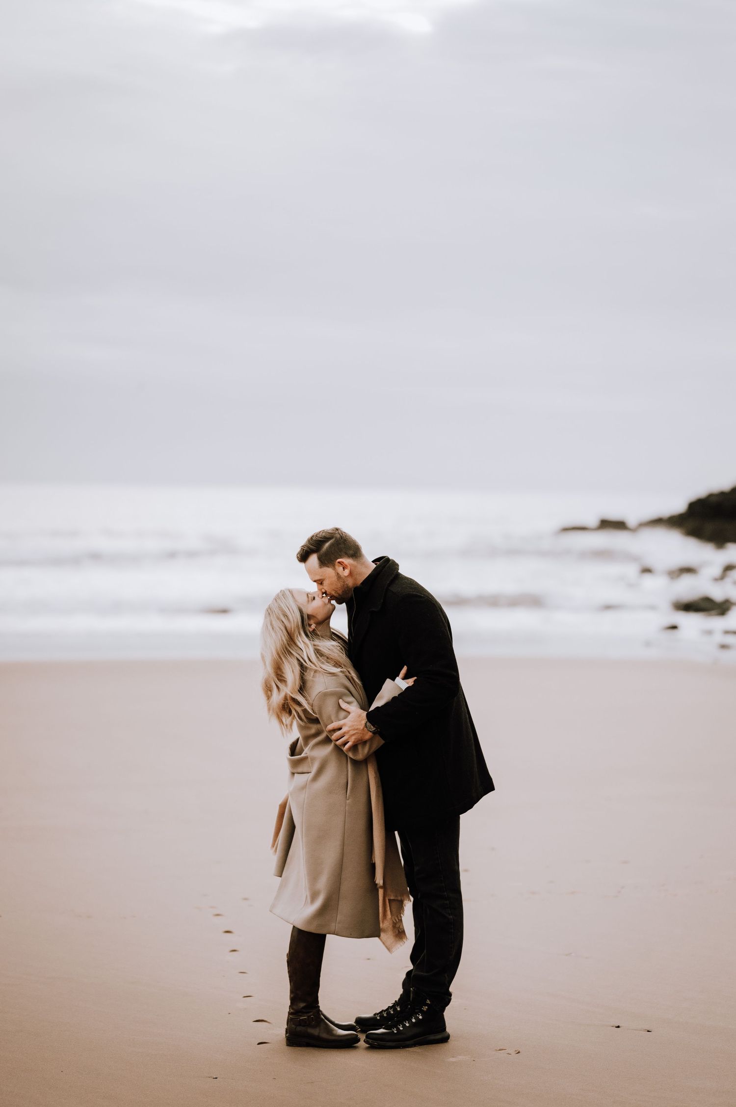 Intimate couple moment on a moody beach with footprints in the sand.