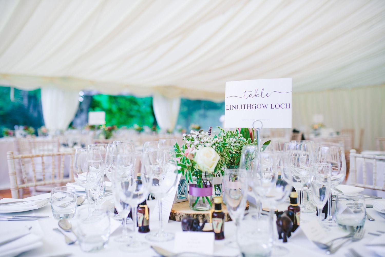Elegant white wedding reception table settings with glassware in a marquee tent.