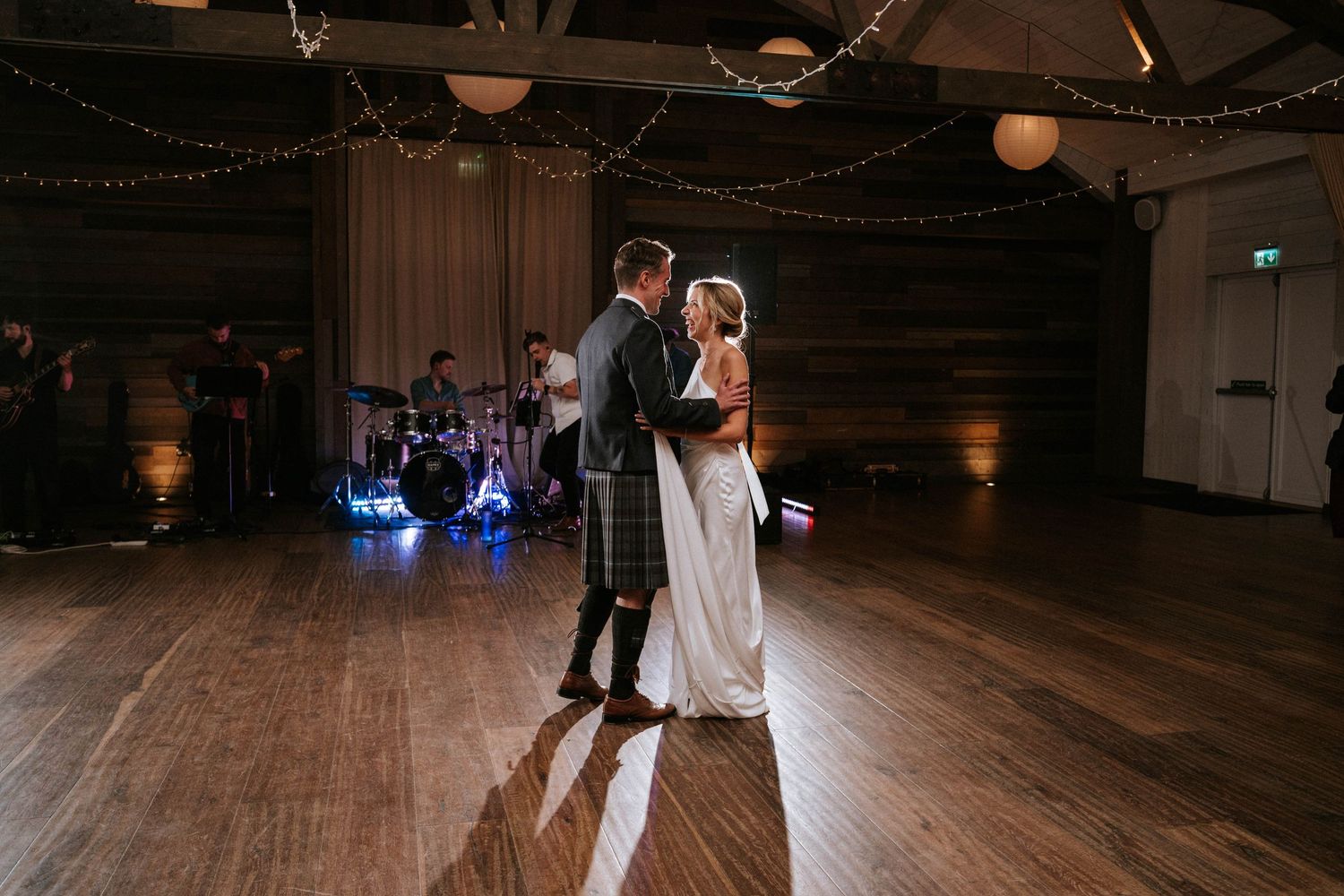 Couple shares first dance on wooden floor under romantic lighting at wedding reception.