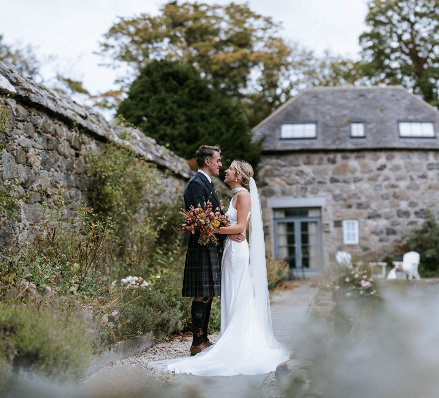 A couple poses for a romantic wedding photo outside a rustic stone cottage in Scotland.