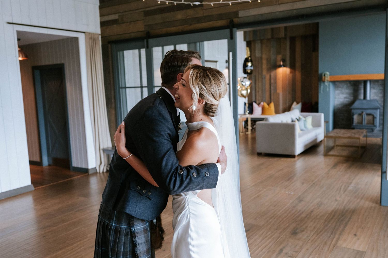 Couple embracing in an indoor venue with wooden floors and large windows.