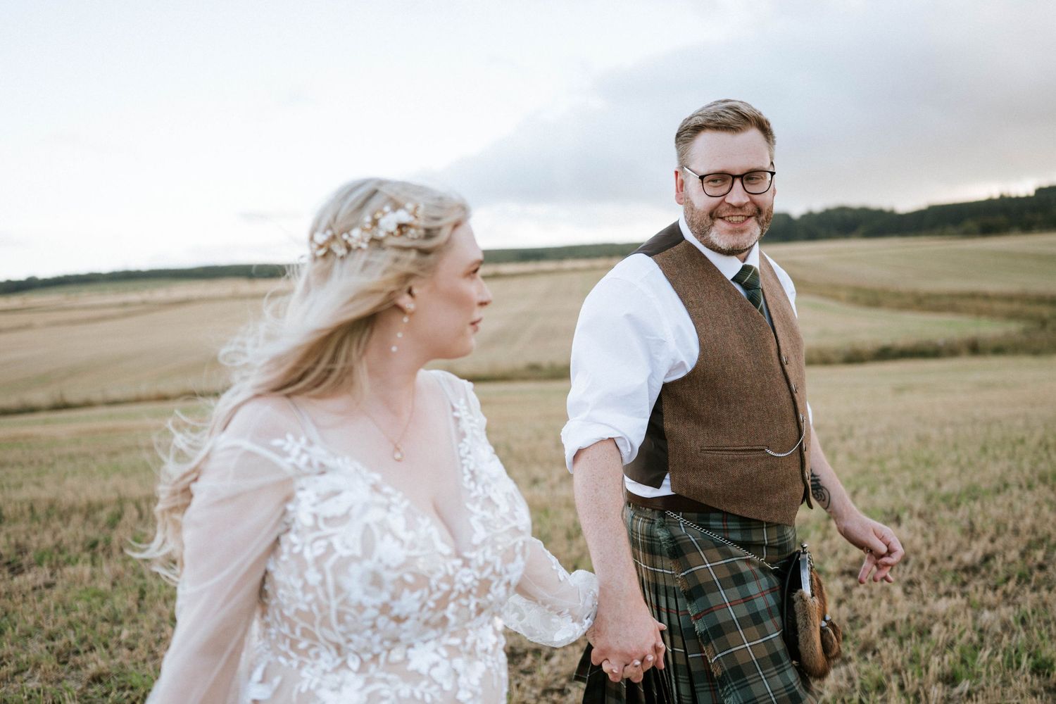 Wedding couple holding hands while walking through golden wheat field.