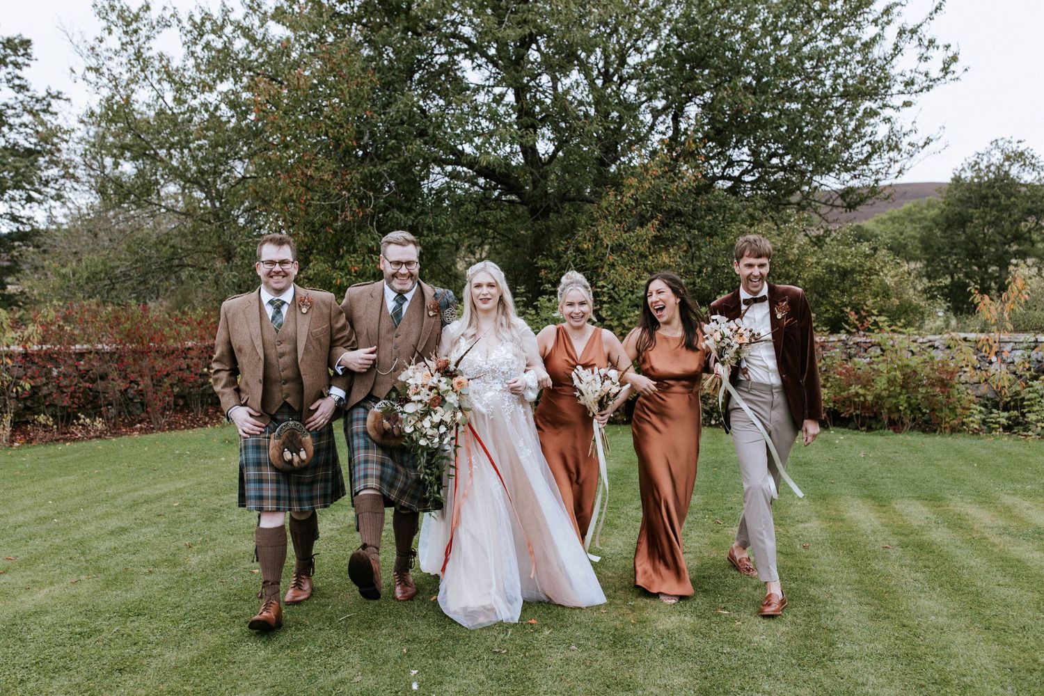 Wedding group photo session on a grassy hillside with Scottish-themed attire.