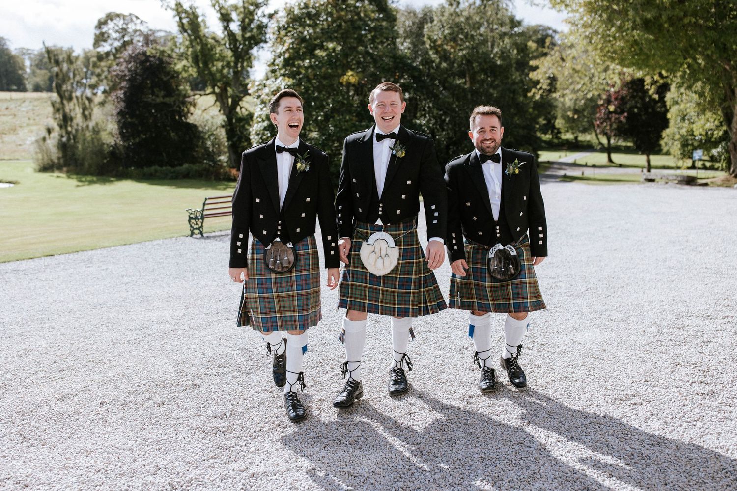 Wedding party walking along a gravel path surrounded by lush green grounds.