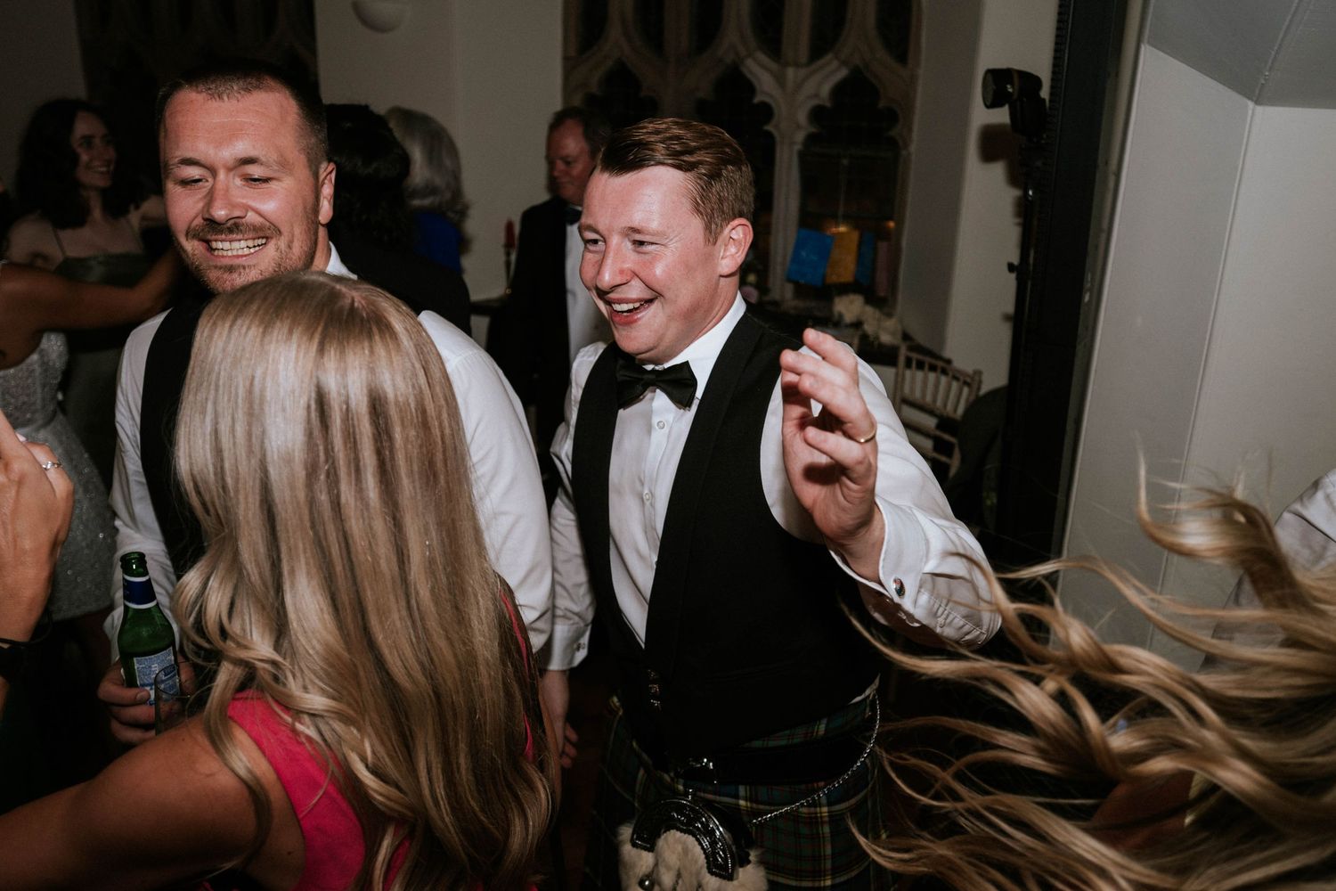 Wedding reception guests dancing and celebrating on a dimly lit dance floor.
