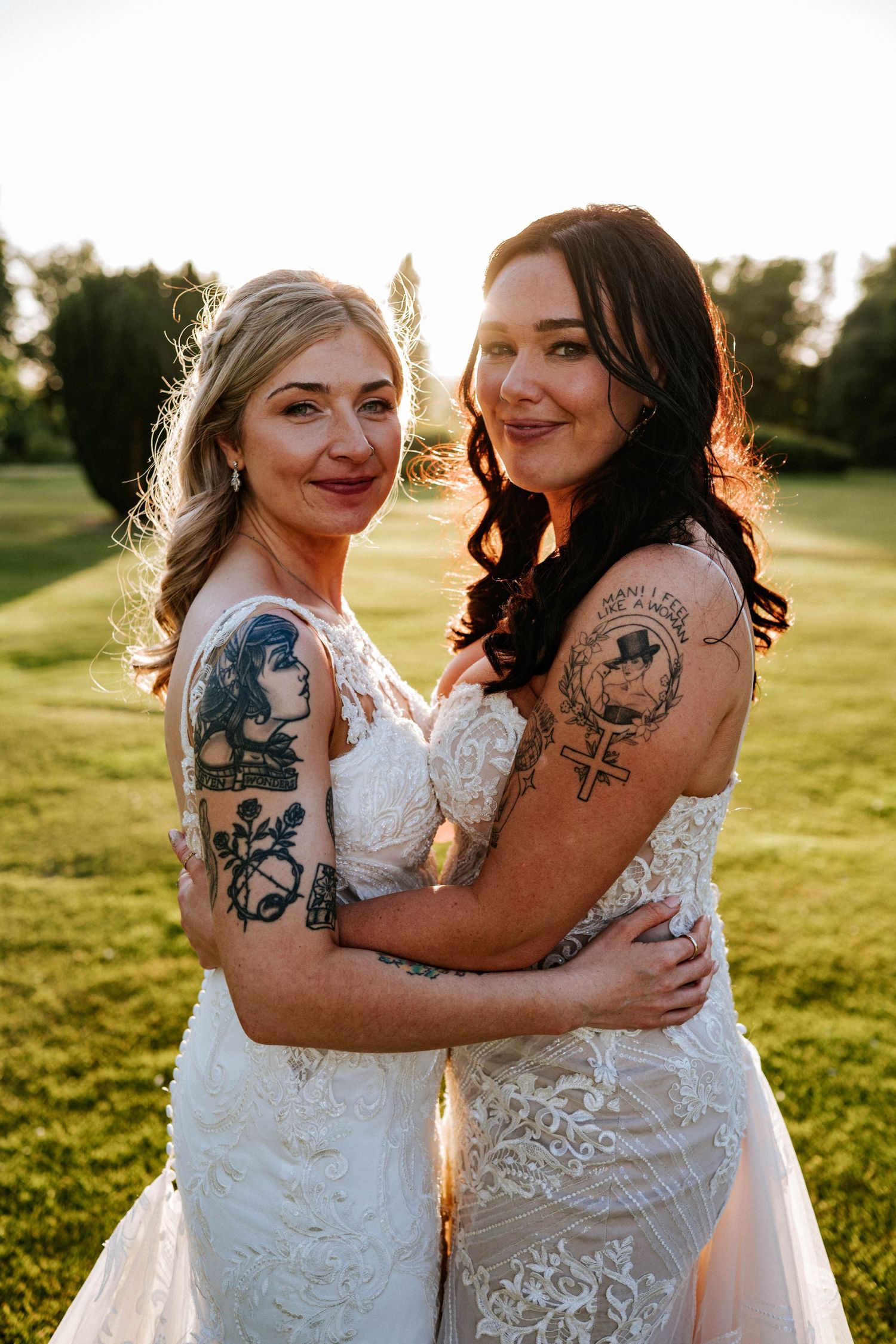 Fasque Castle Wedding Photography. Close-up of two people in white lace dresses showing their tattoos while embracing outdoors.