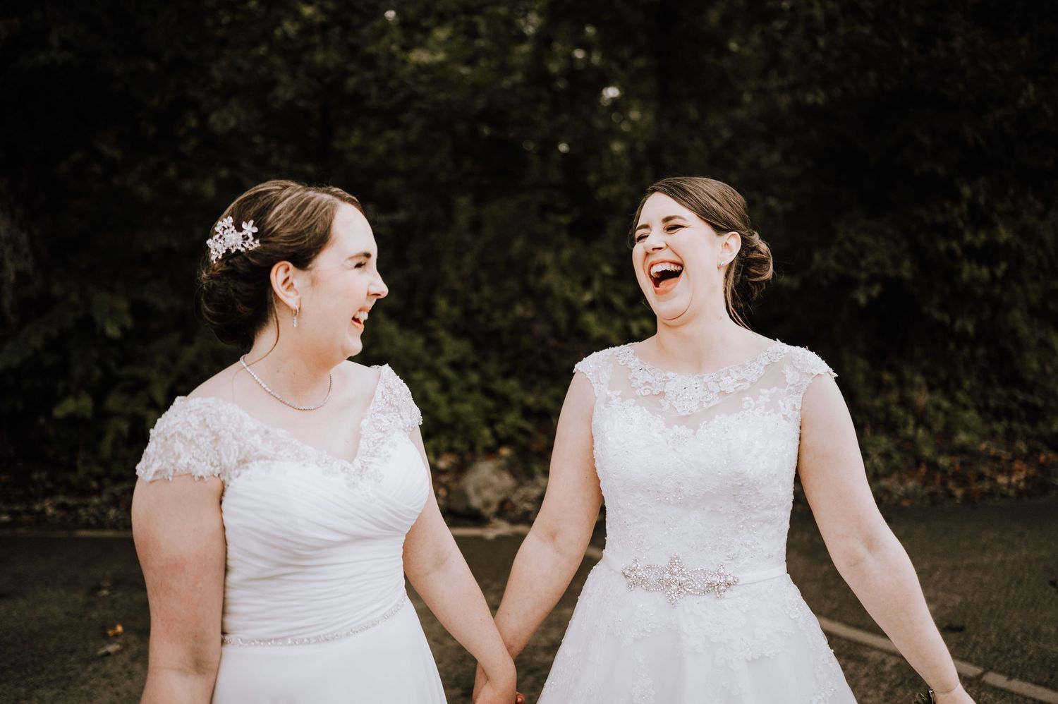 Two people in elegant white wedding gowns laugh together during an outdoor photo session. Meldrum House Wedding Photography.