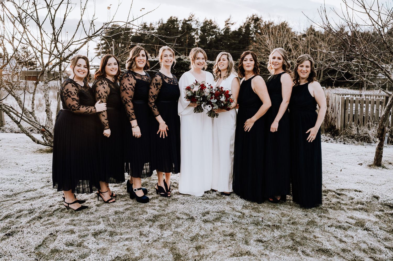Same Sex Wedding Photography. Wedding party in black dresses poses with couple in white against snowy landscape.
