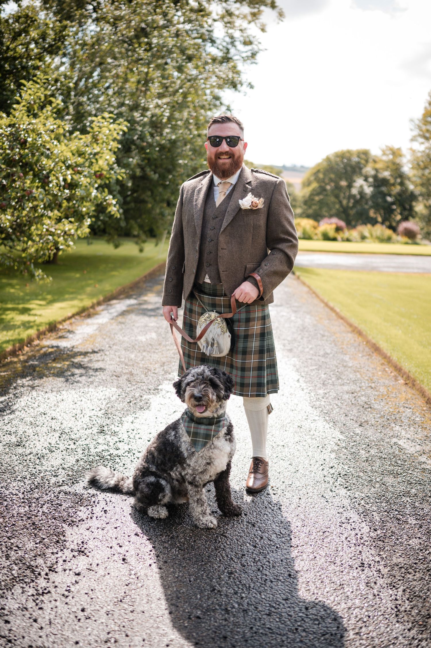 Aberdeen Wedding Photography. Scottish terrier dog poses with person wearing traditional kilt on gravel path.