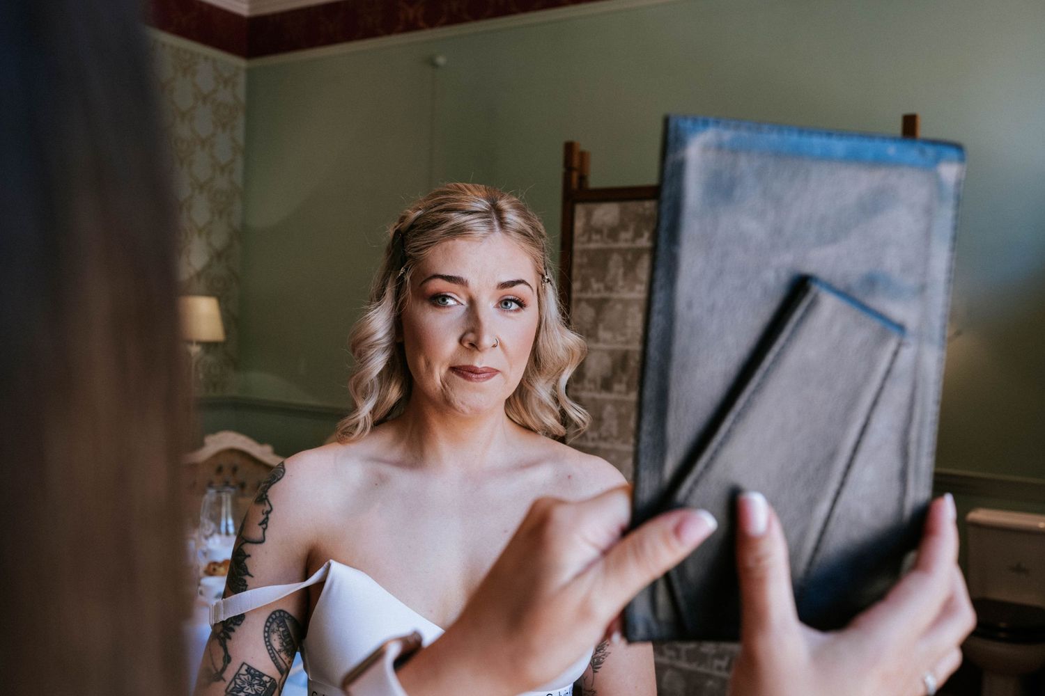 A person in a white dress looks at their reflection while getting ready.