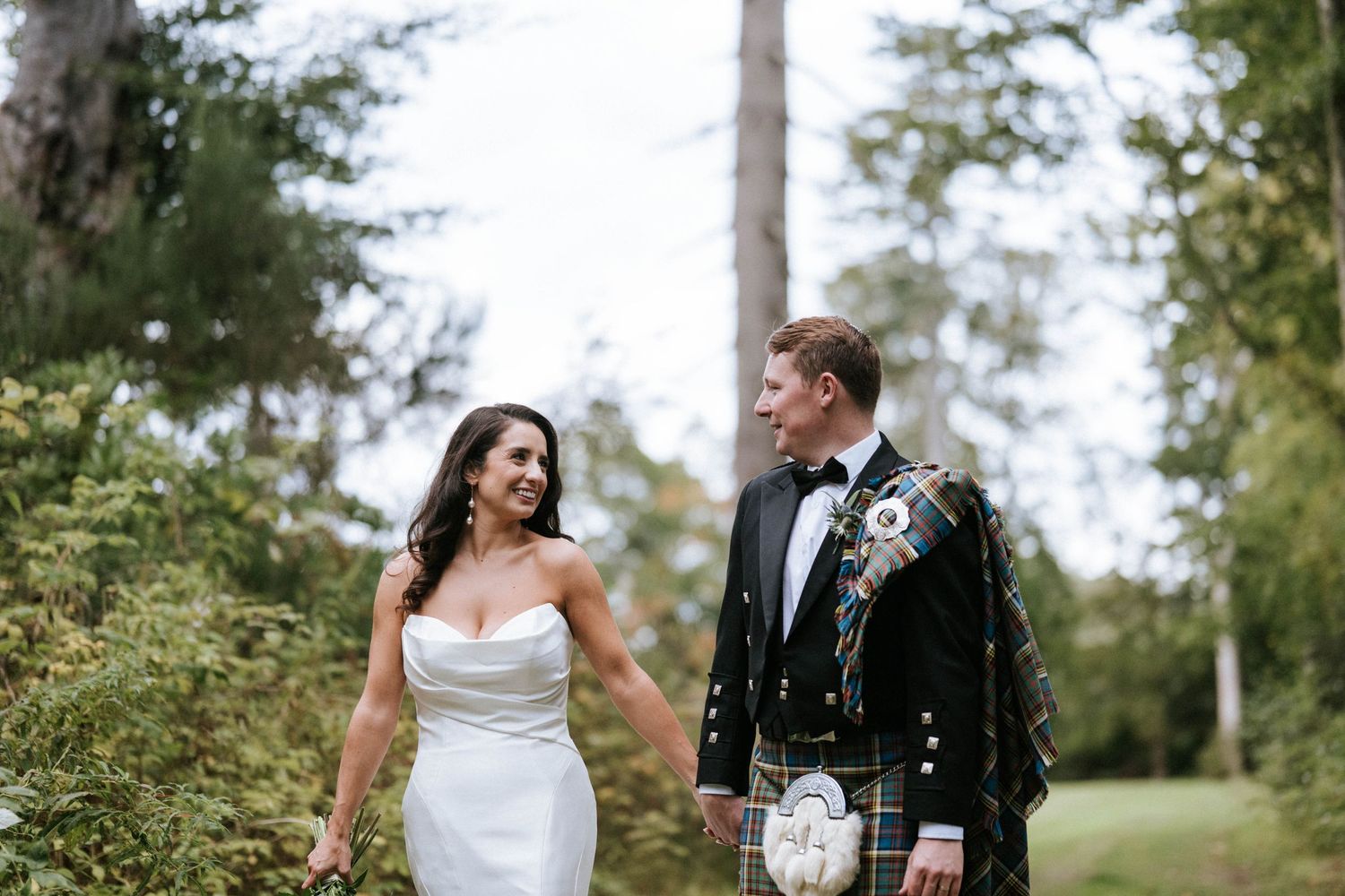 Wedding couple shares a candid moment outdoors with groom wearing traditional Scottish formal wear.