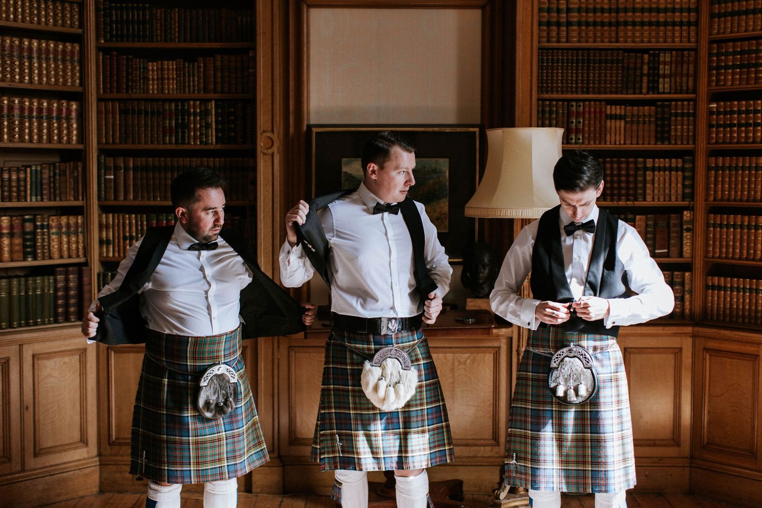 Groomsmen in traditional Scottish kilts and formal wear gathered in a classic library.