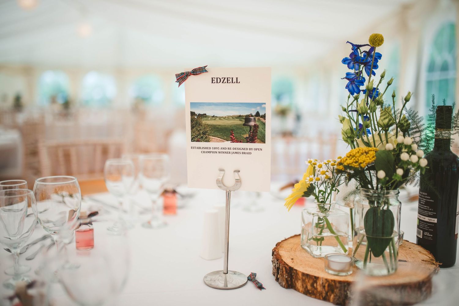 Wedding table centerpiece with wildflowers on wood slice and postcard table number in marquee setting.
