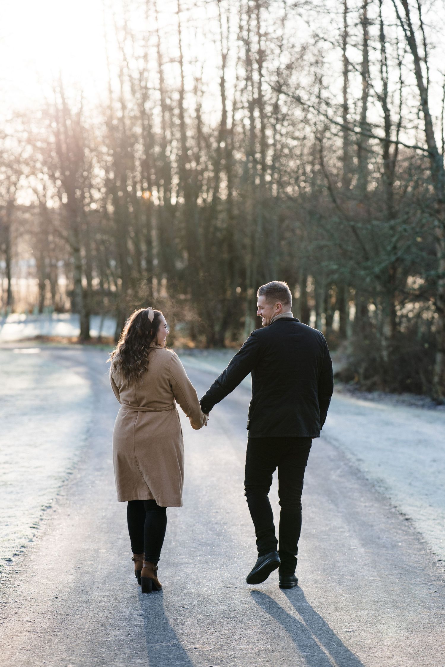 Couple walking hand in hand down snowy winter path at sunset.